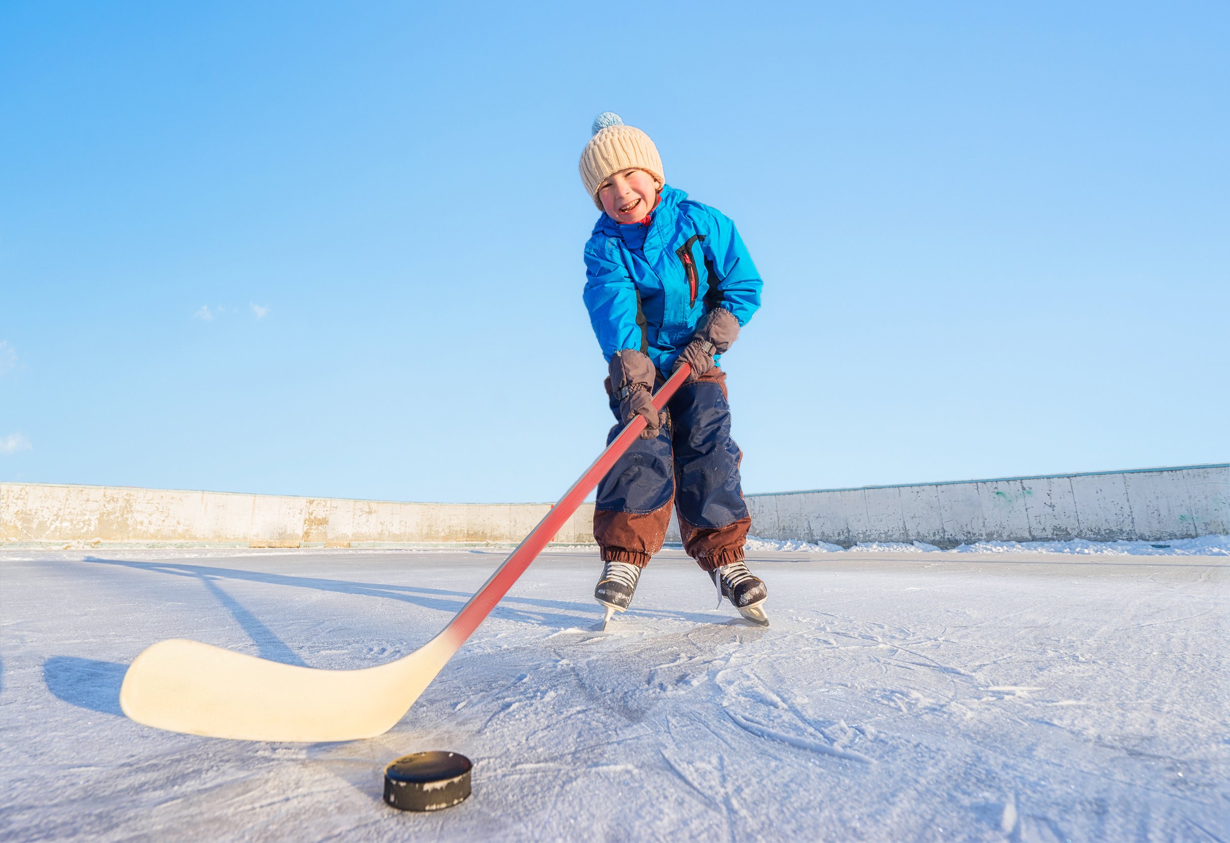 Child ice skating with a hockey stick and puck outdoors on a rink.