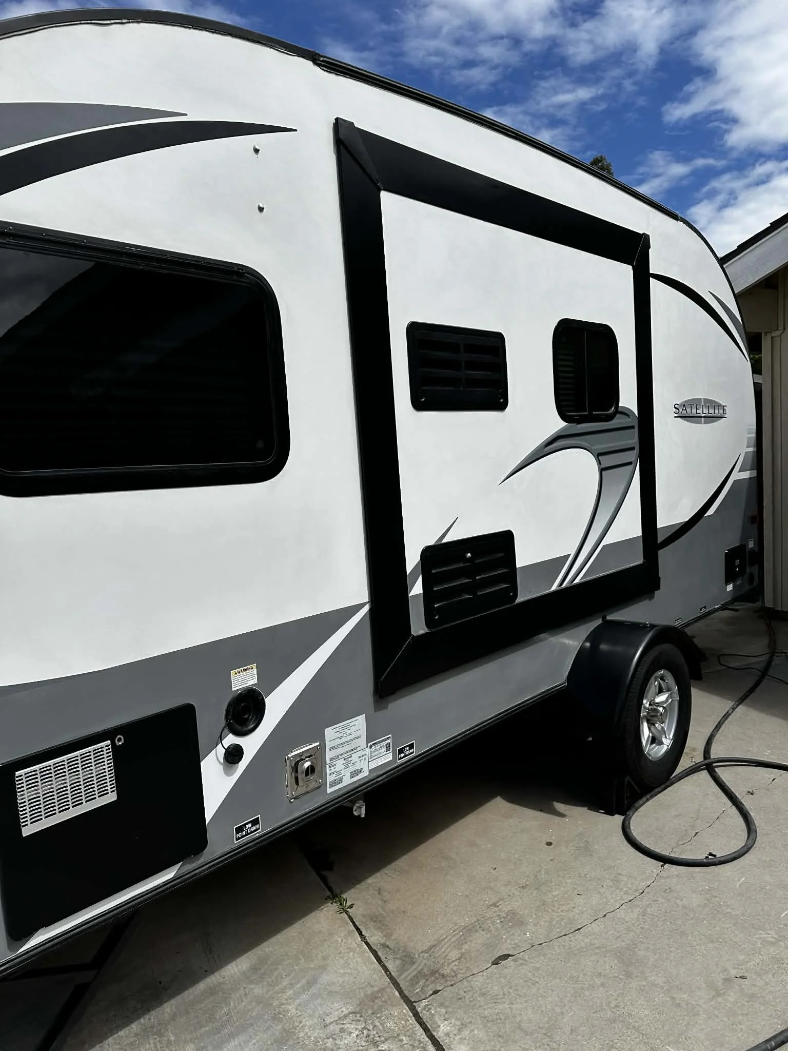 Side view of a white and black travel trailer with windows, ventilation, and an attached power cord, parked on concrete.