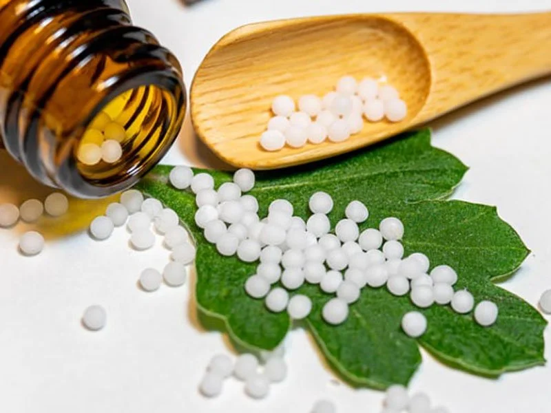 Homeopathic pellets on green leaf with wooden spoon and brown bottle