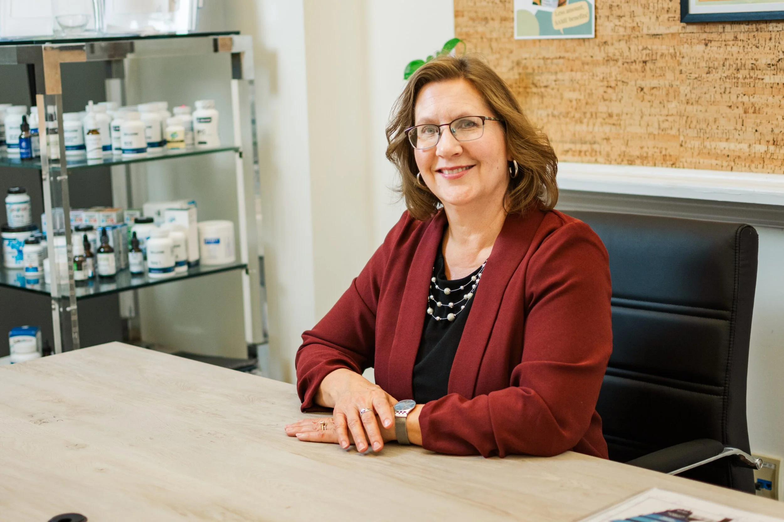 Person sitting at a desk in an office with shelves of bottles.