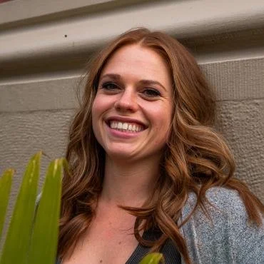 Woman smiling outdoors near a wall with greenery