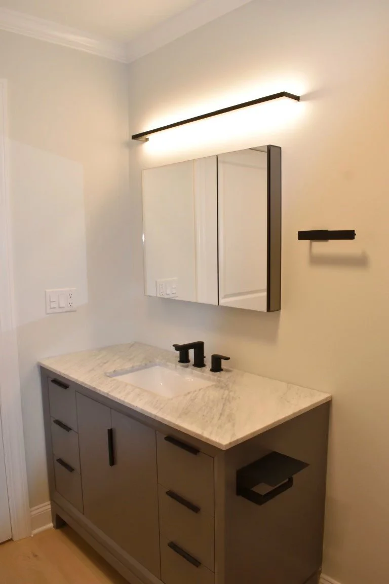 Modern bathroom vanity with a beige marble countertop, black fixtures, a white undermount sink, a gray cabinet with black handles, a mirrored medicine cabinet, and a black horizontal wall light fixture.