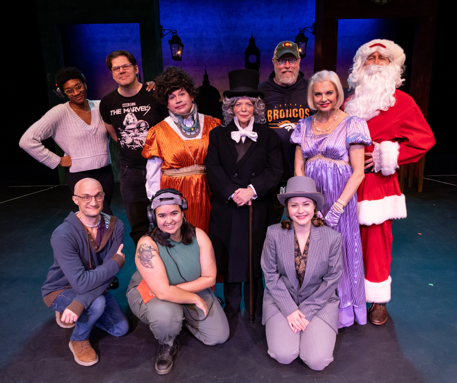 The cast and director of “The Farndale Avenue Housing Estate Townswomen’s Guild Dramatic Society’s Production of ‘A Christmas Carol’” pose onstage at the Aurora Fox, smiling toward the camera.