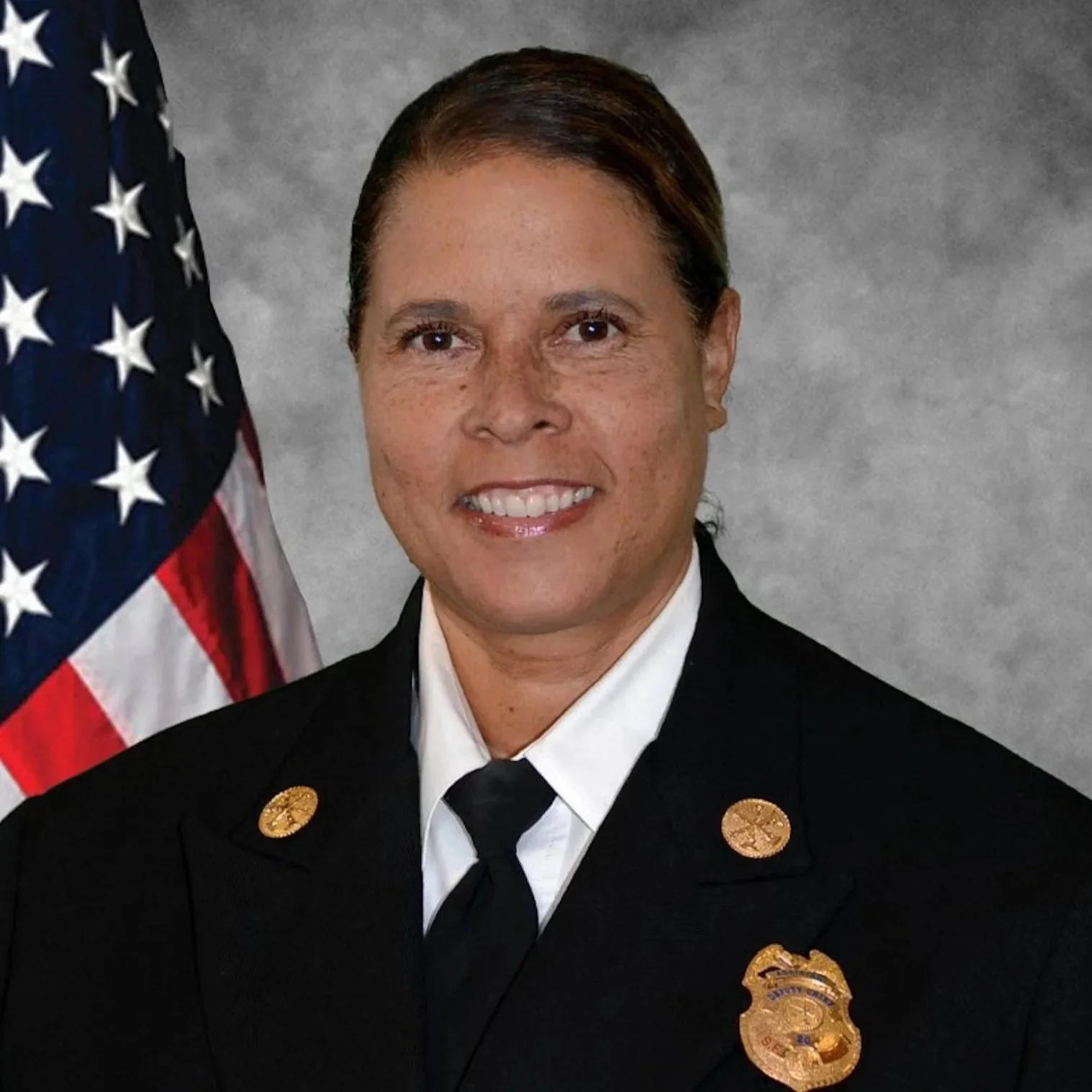 A female firefighter in uniform standing next to an American flag.