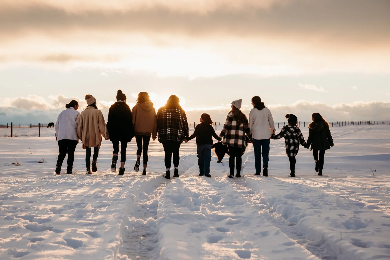 A line of girls walking together across the snow at sunset