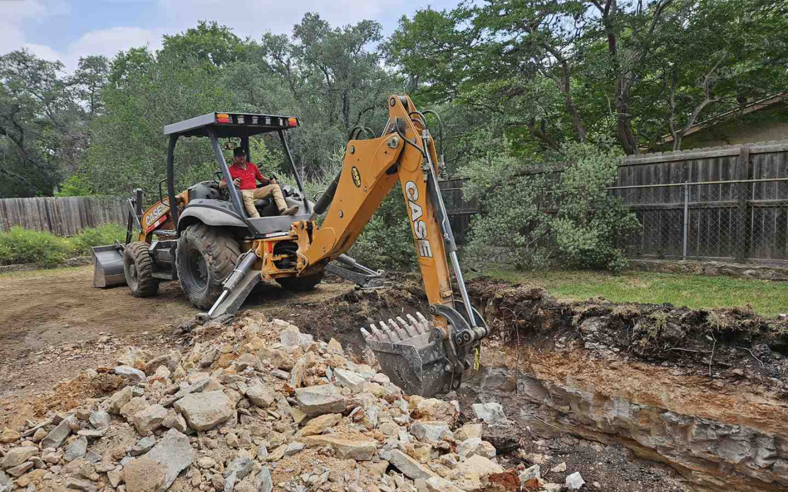 Excavator digging through rocky ground during septic system site preparation.