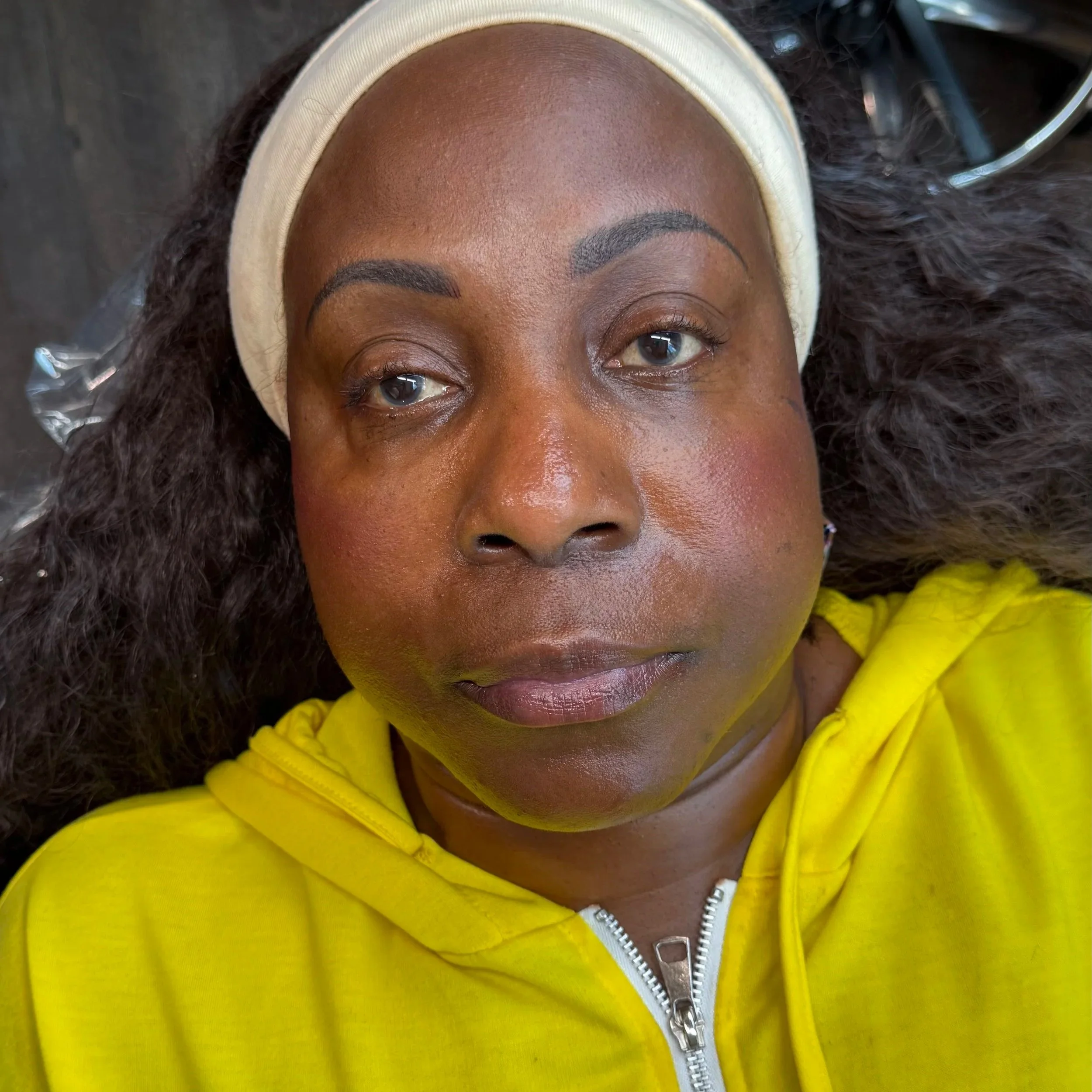 Close-up of a woman with dark skin wearing a yellow hoodie, lying on her back with curly hair surrounded by a headband and a hair wrap.
