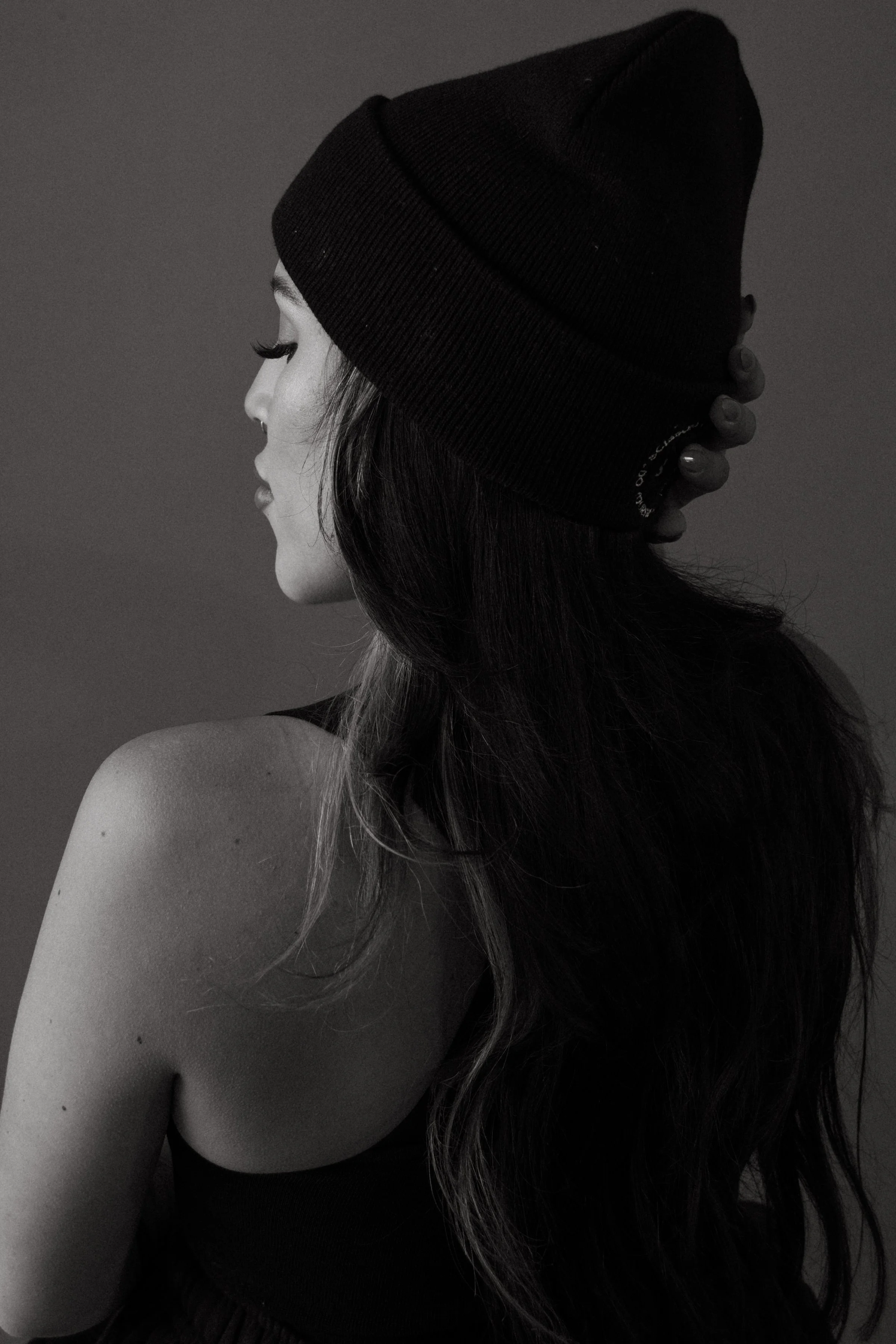 Side profile of a woman with long hair, wearing a black beanie and a black top, with the focus on her face and shoulder in a black and white photo.