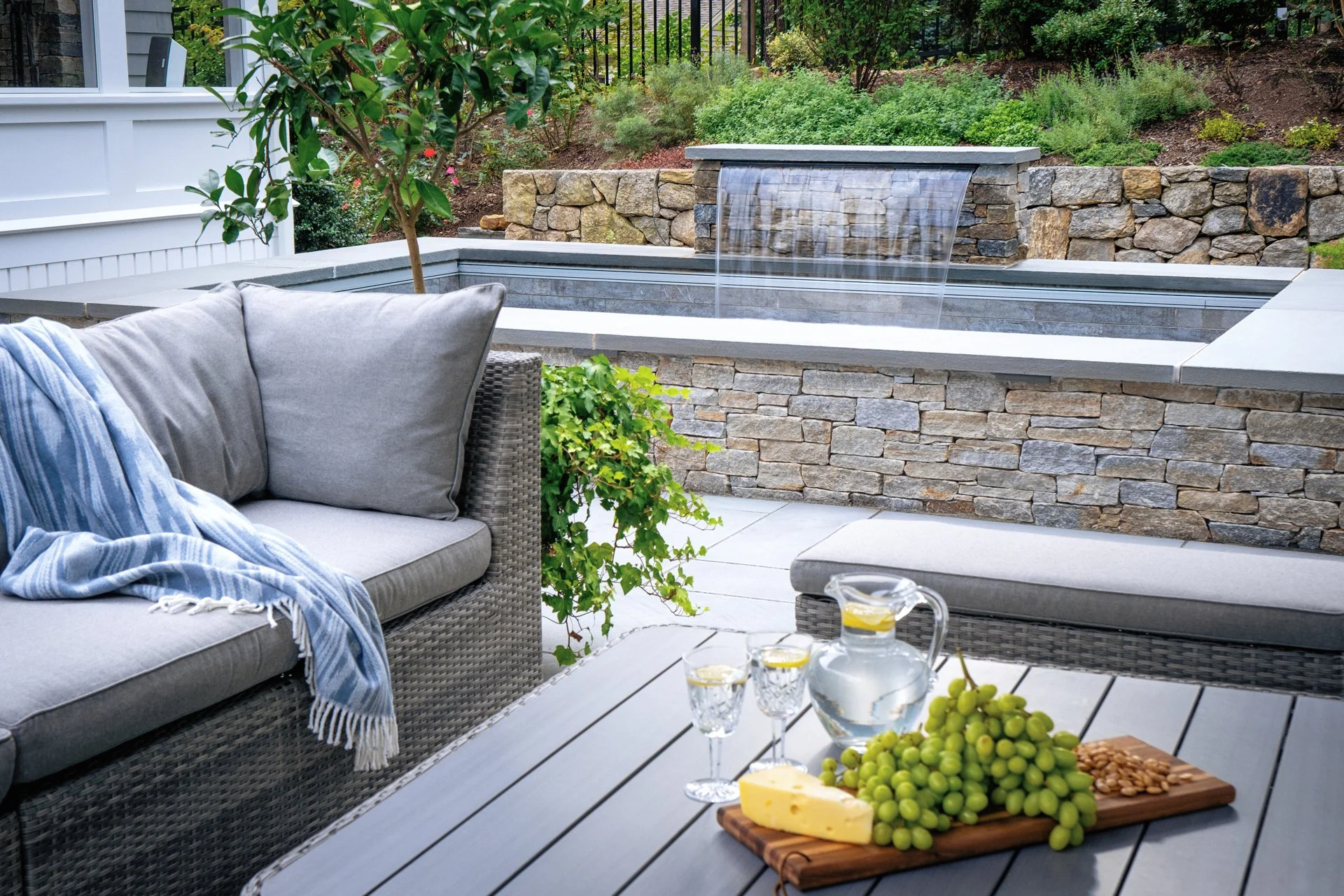 [small-spaces][raised]COMPACT SOAKE POOL WITH A CASCADING WATERFALL, NATURAL STONE SURROUND, AND CUSHIONED PATIO SEATING.