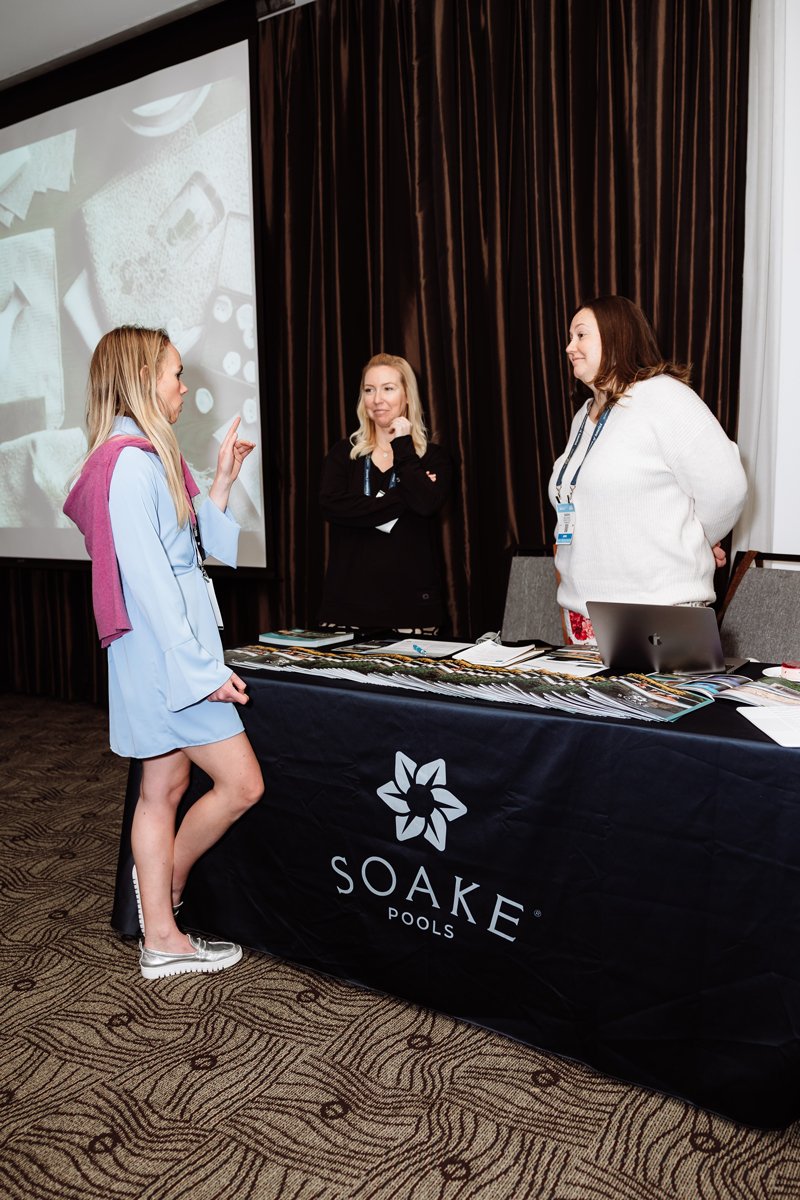 Soake Pools team speaking with an attendee at a design conference booth, showcasing plunge pool solutions.