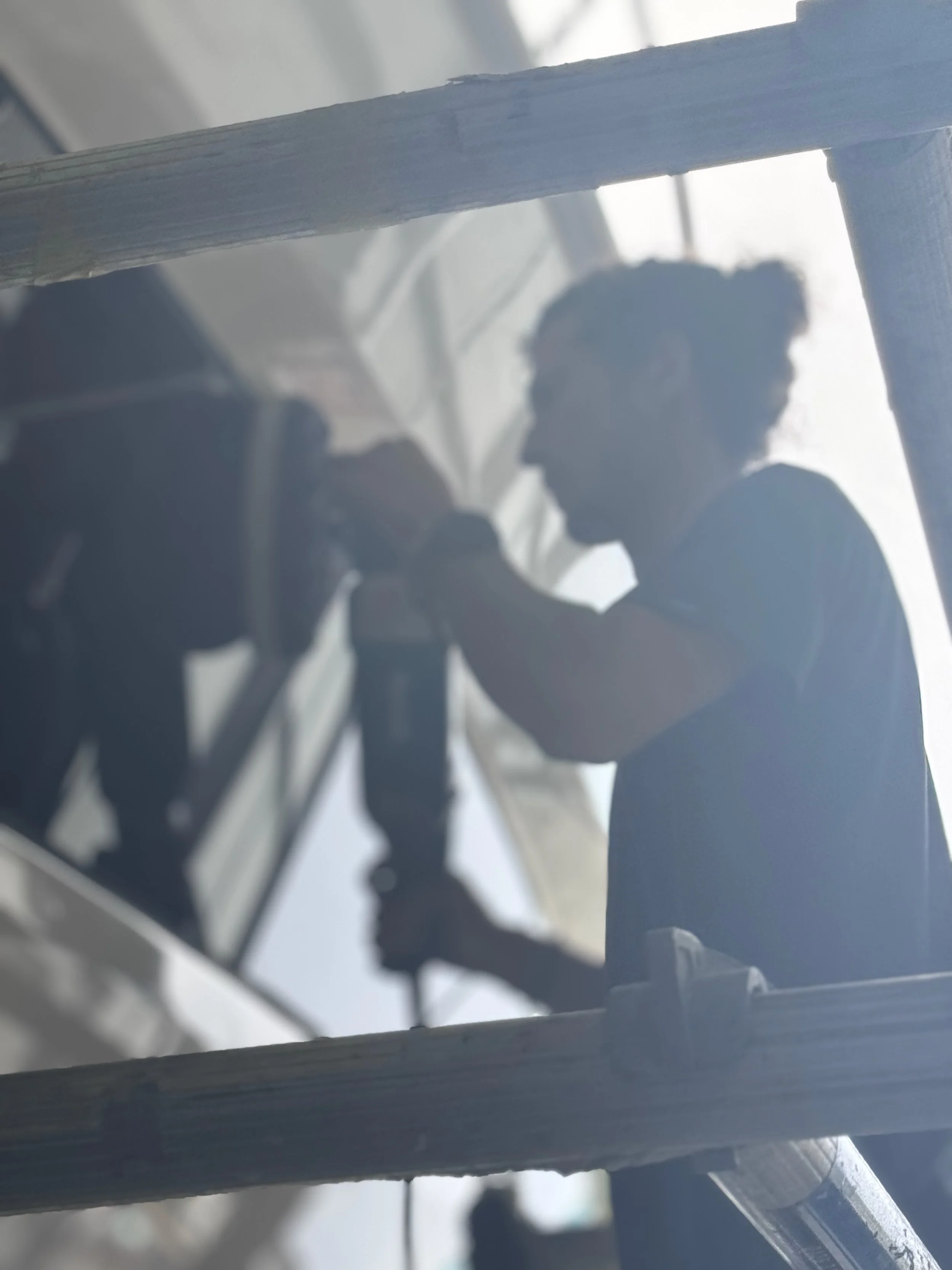 Silhouette of a person painting or working on a ceiling, viewed from below through a wooden frame.
