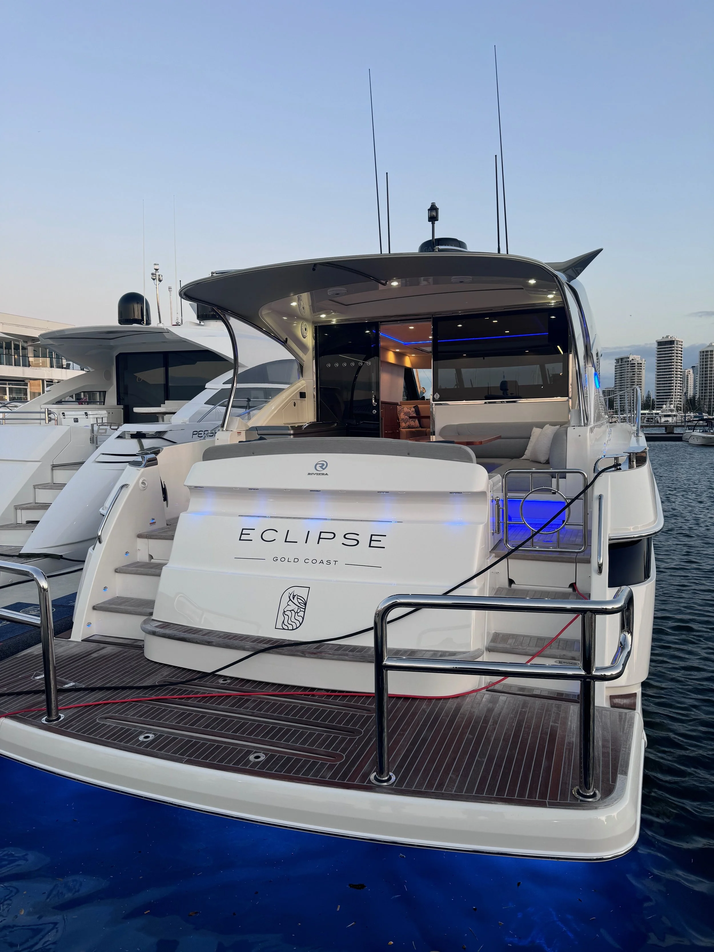 Luxury yacht named Eclipse docked at a marina, showcasing a spacious deck with stainless steel railings and modern amenities, with city skyline in the background.