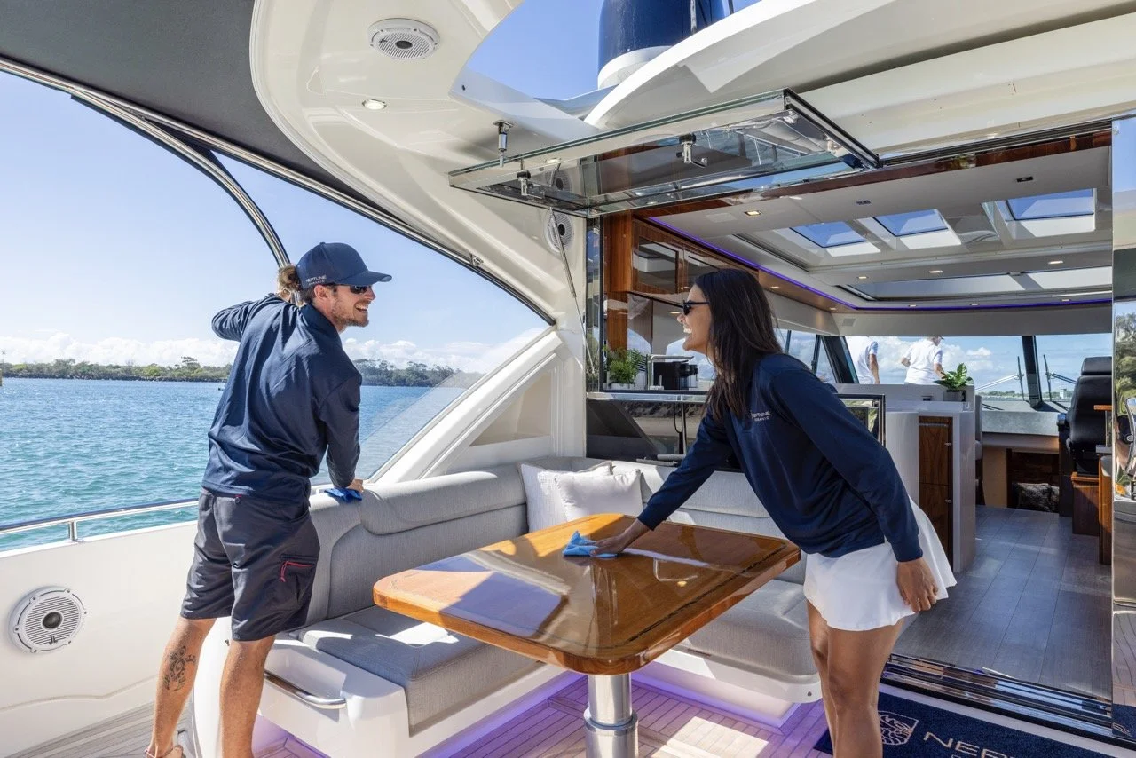 Two people cleaning a yacht's interior with a view of water and sky outside.