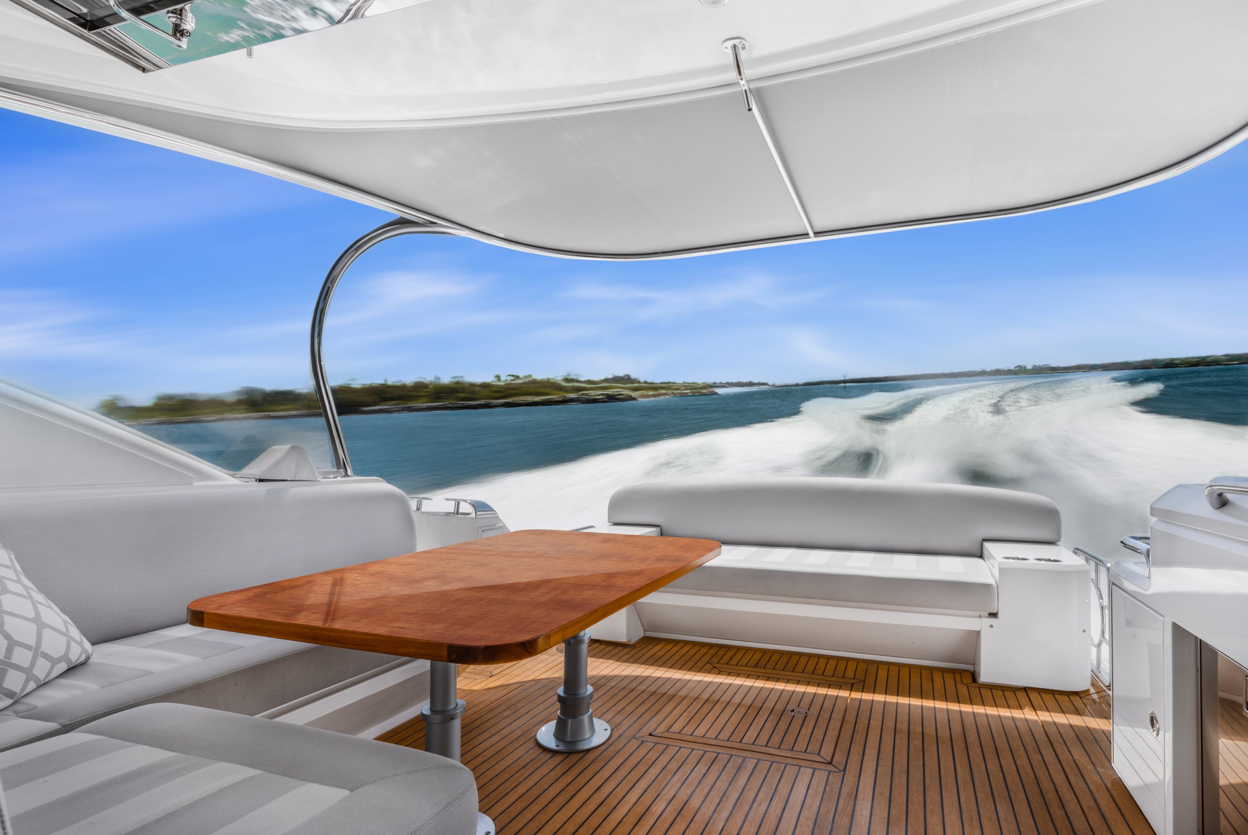 Yacht deck with white seating, a wooden table, and a view of the water and shoreline in the distance.