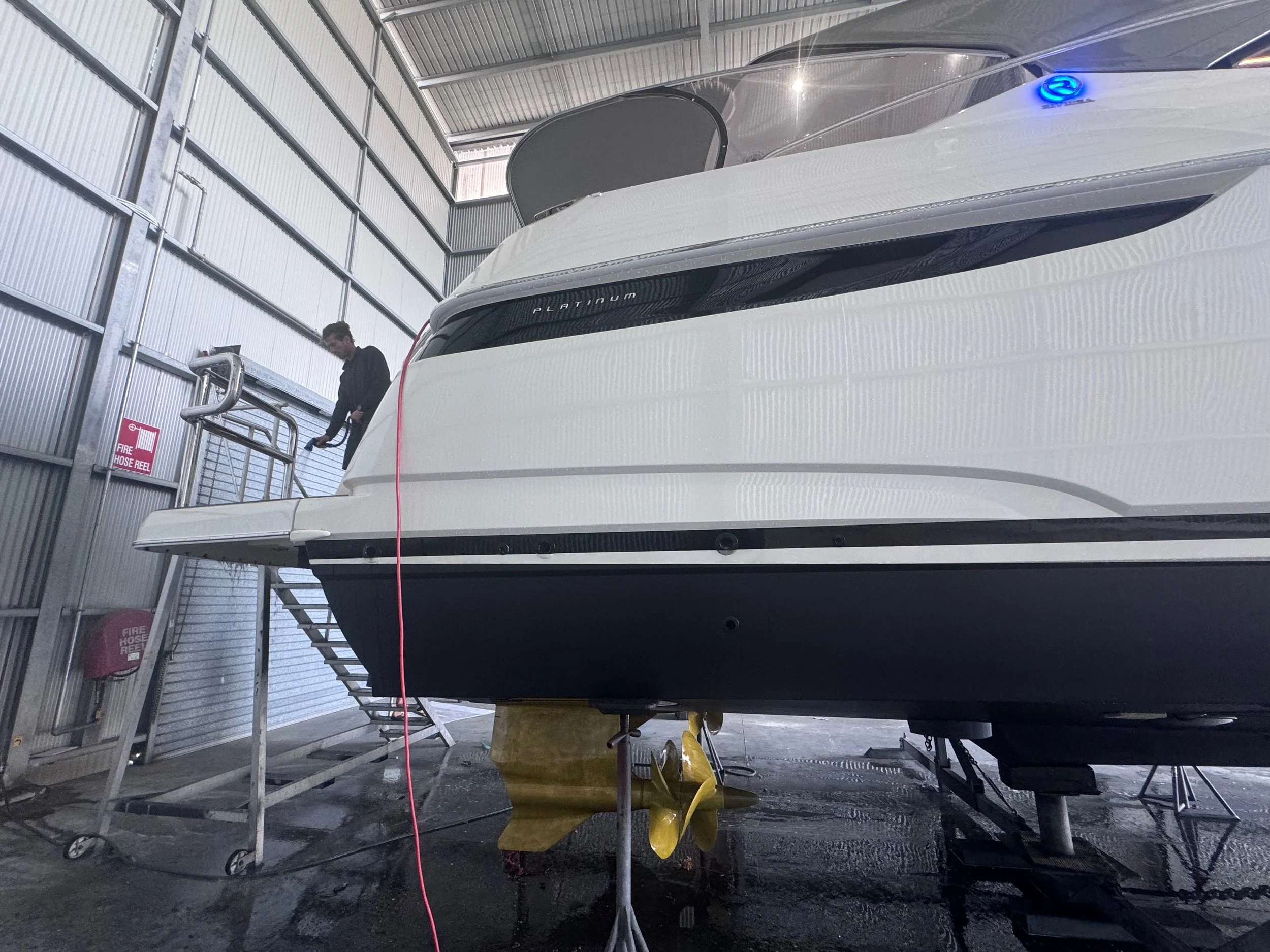 A person standing on a set of stairs next to a large white yacht inside a boat storage facility.