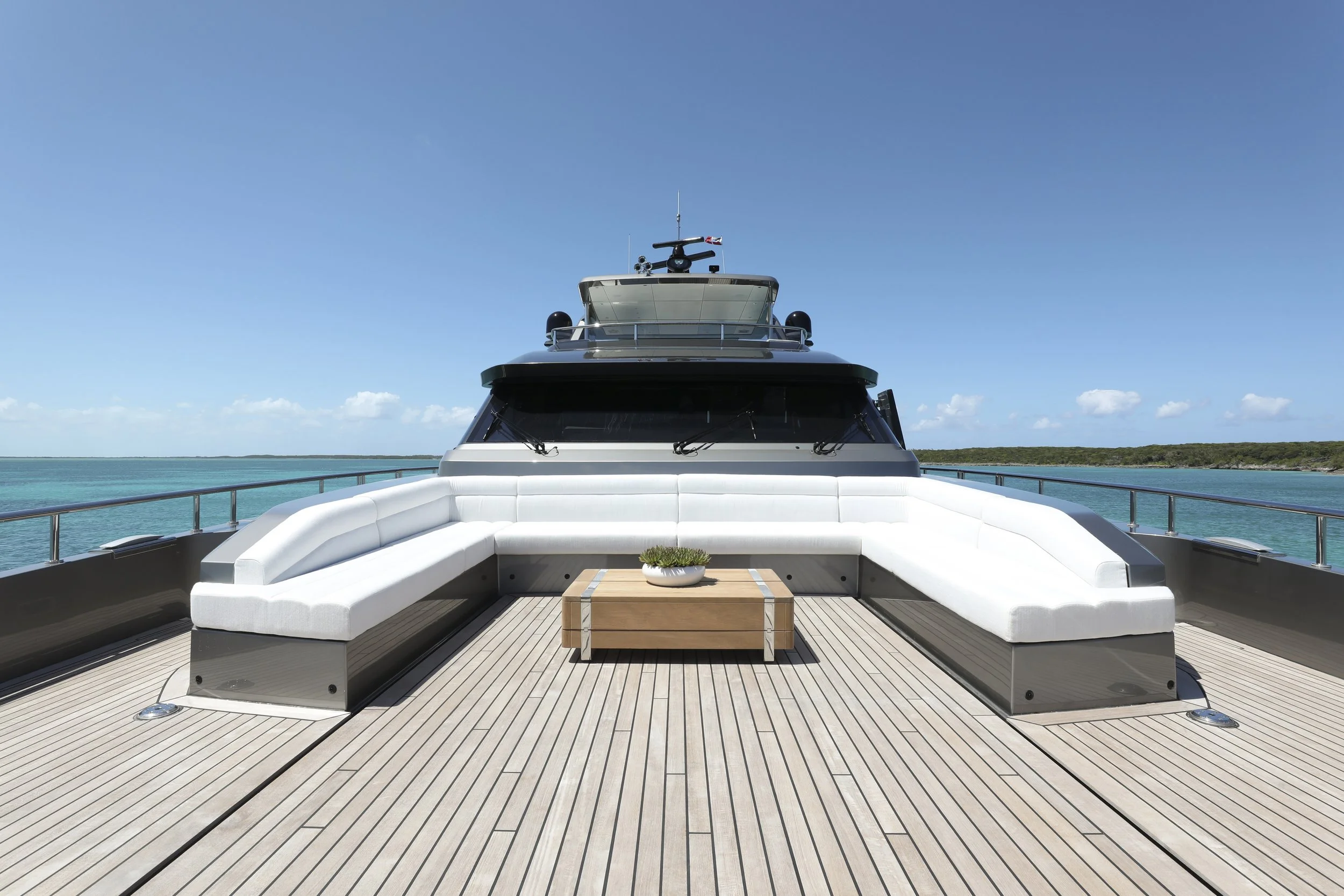 Front view of a luxurious yacht with white seating area and small wooden table on deck, ocean and clear blue sky in background.