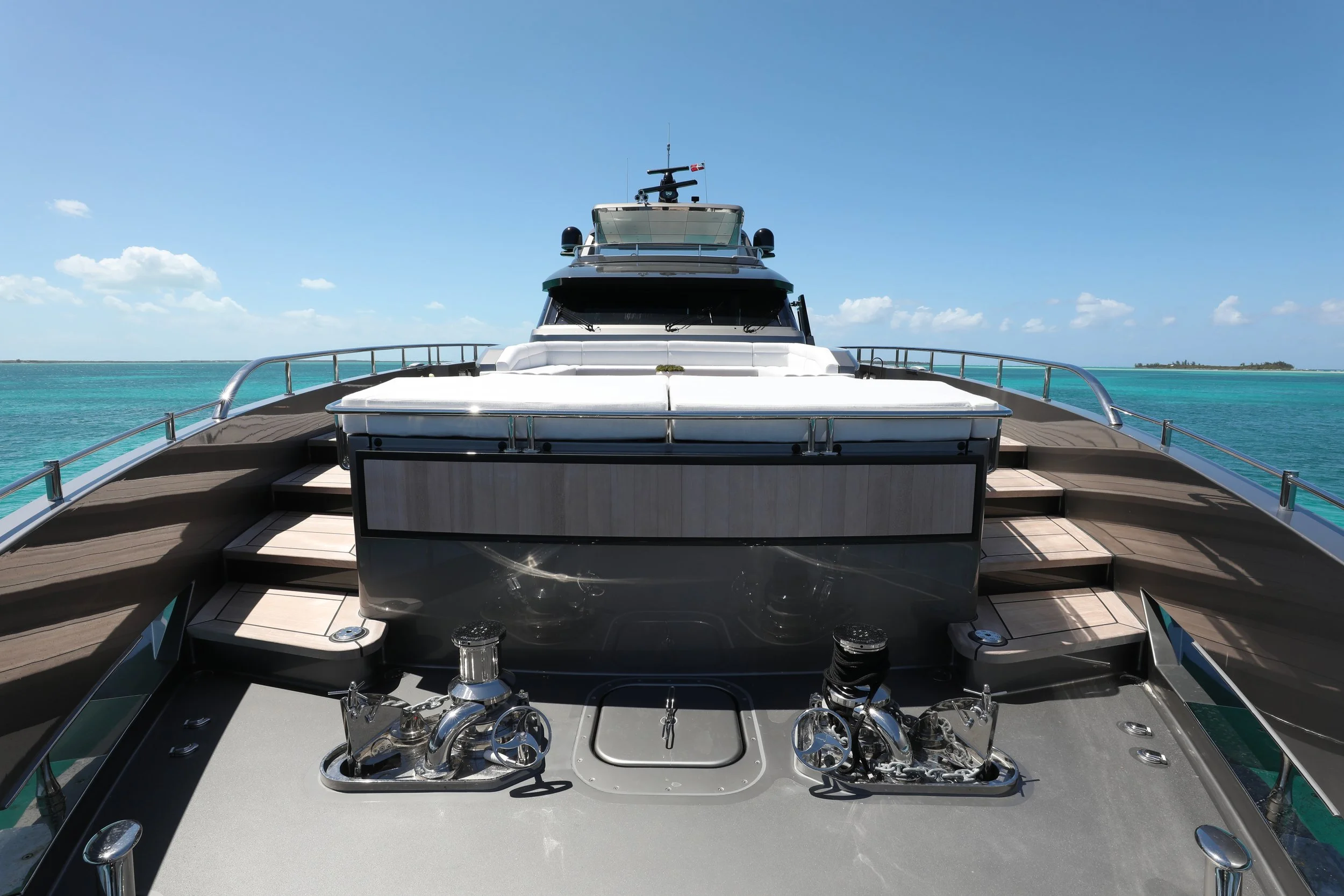 Front view of a luxury yacht on clear turquoise water under a blue sky with scattered clouds.