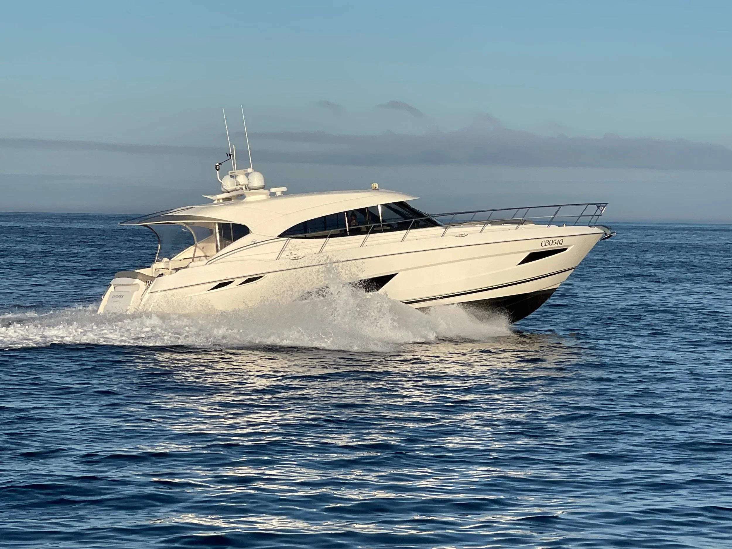 A white yacht sailing on calm ocean waters under a blue sky.
