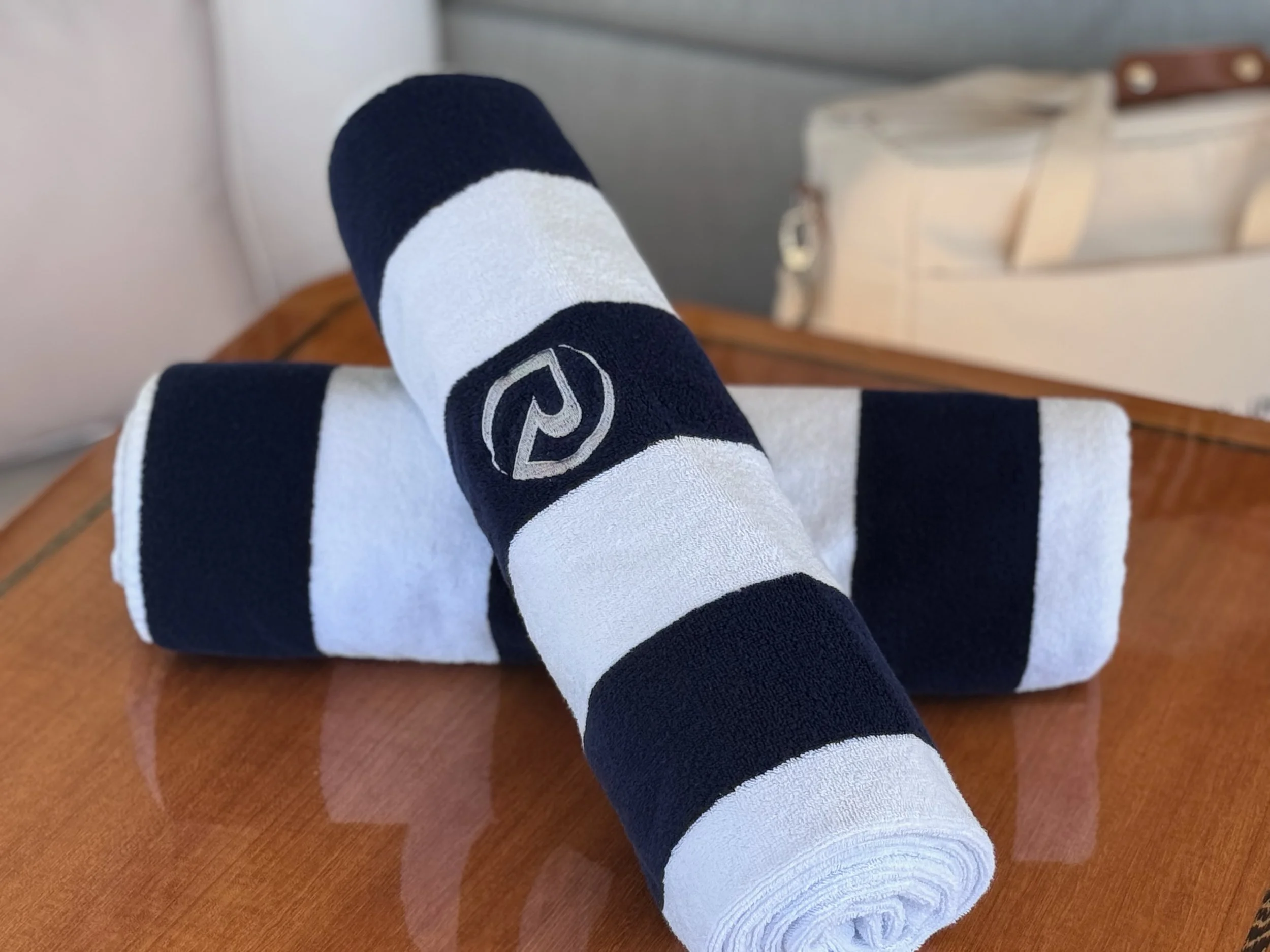 Two rolled tennis towels with a navy blue and white striped pattern, featuring a logo on one towel, placed on a wooden surface.