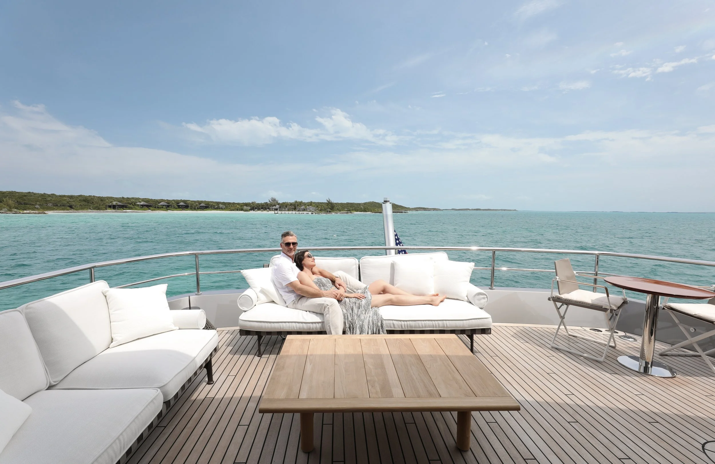 Couple relaxing on a yacht's deck with ocean and coastline in the background