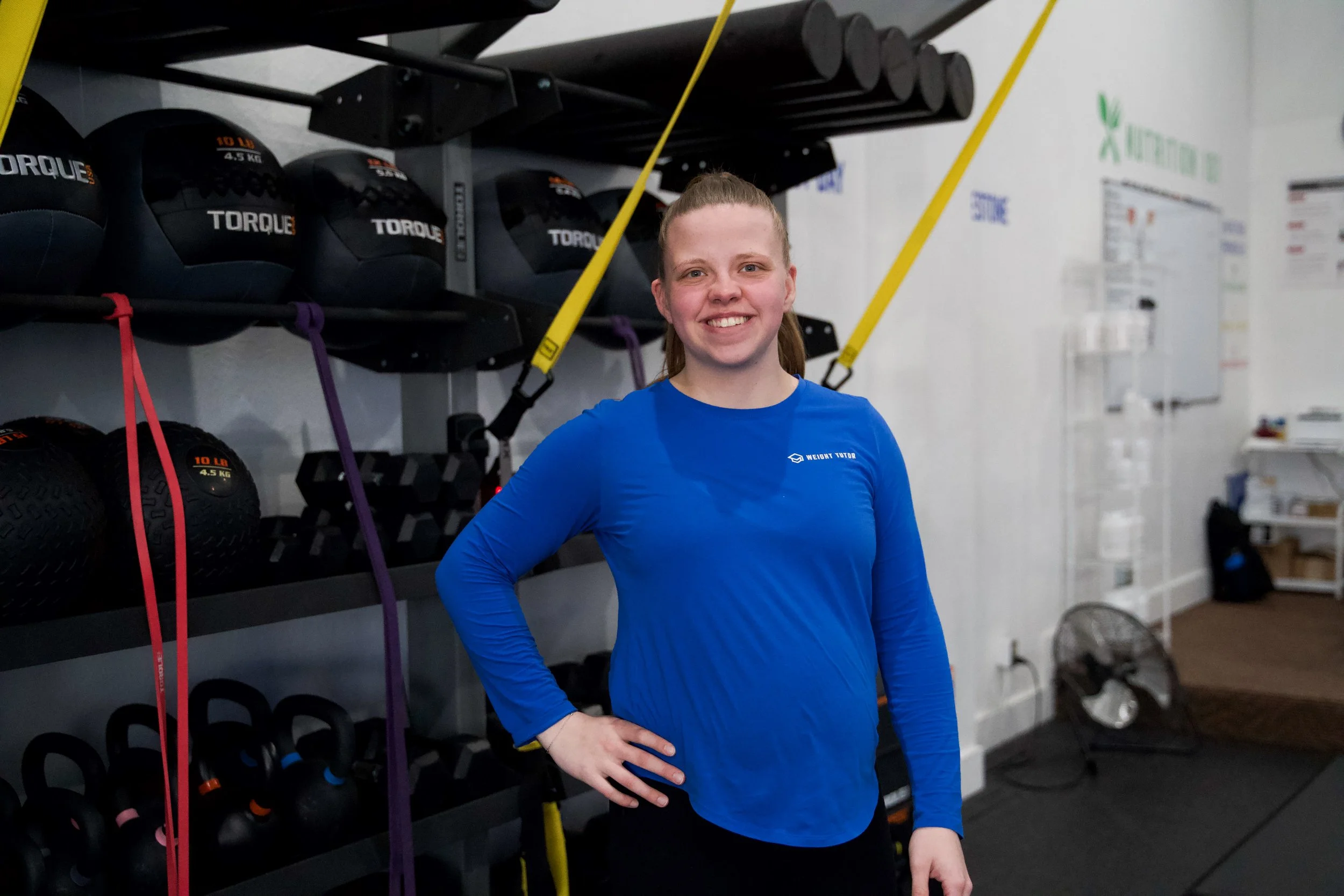 Young woman smiling in a blue workout jacket in a gym.