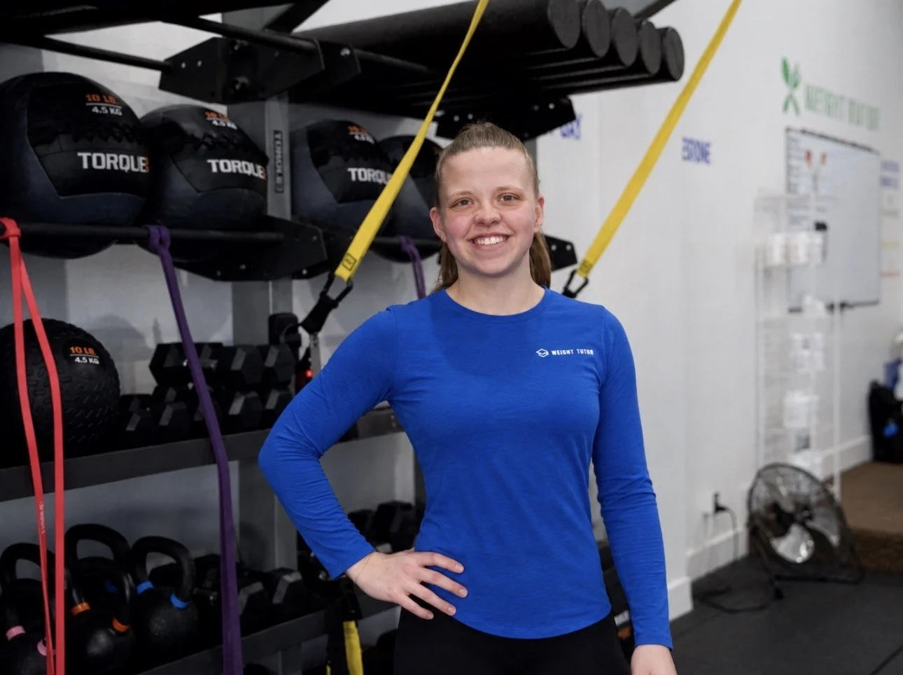 Young woman smiling in a blue workout jacket in a gym.