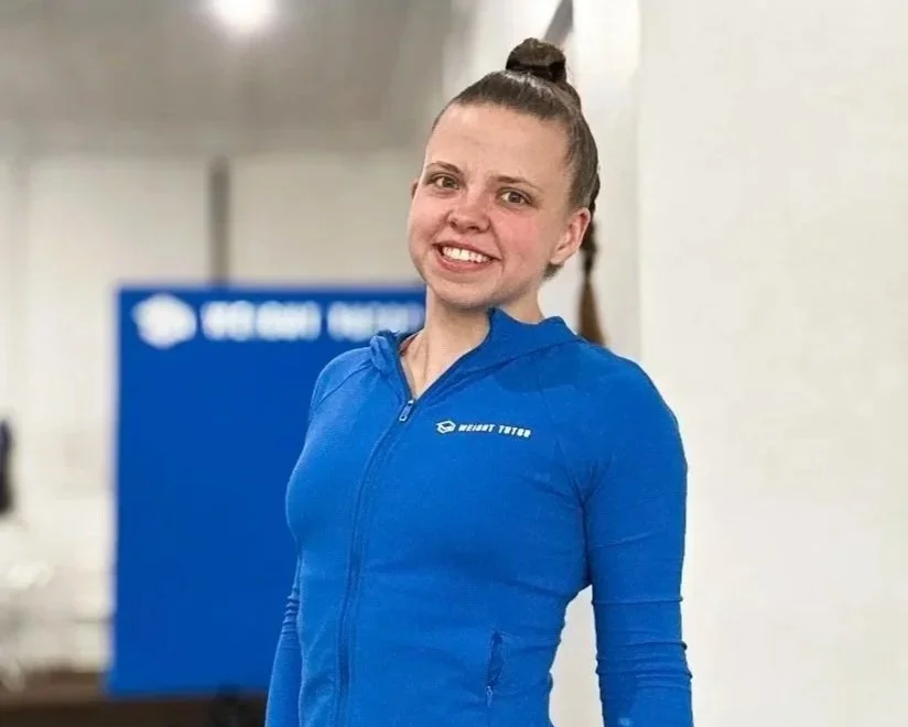 Young woman smiling in a blue workout jacket in a gym.