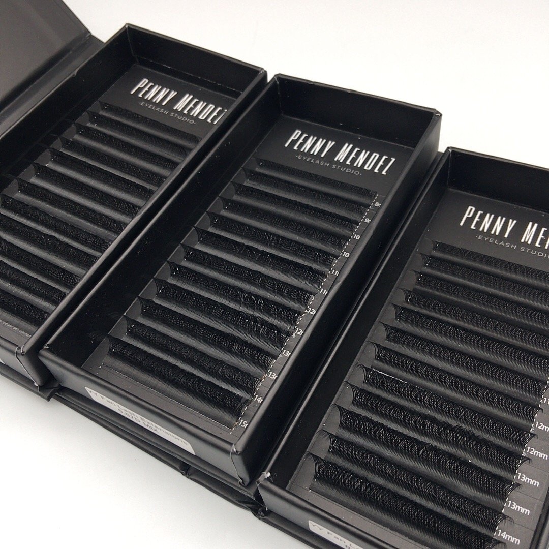 Tres cajas negras con pestañas de distintas longitudes y grapas, destinadas para extensiones de pestañas, con la marca Penny Mendez - Eyelash Studio.