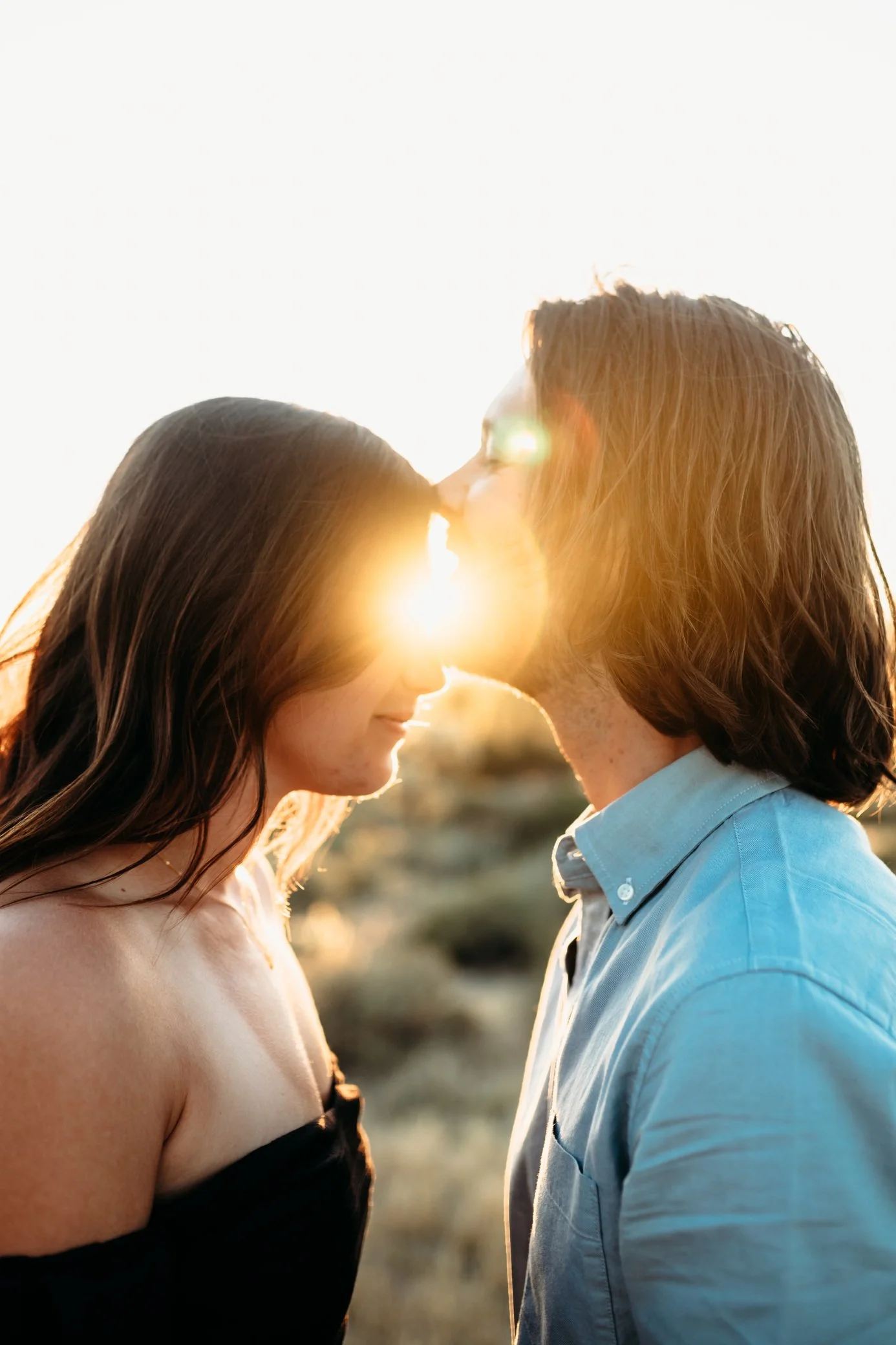 boyfriend kissing girlfriend on forehead with sun behind