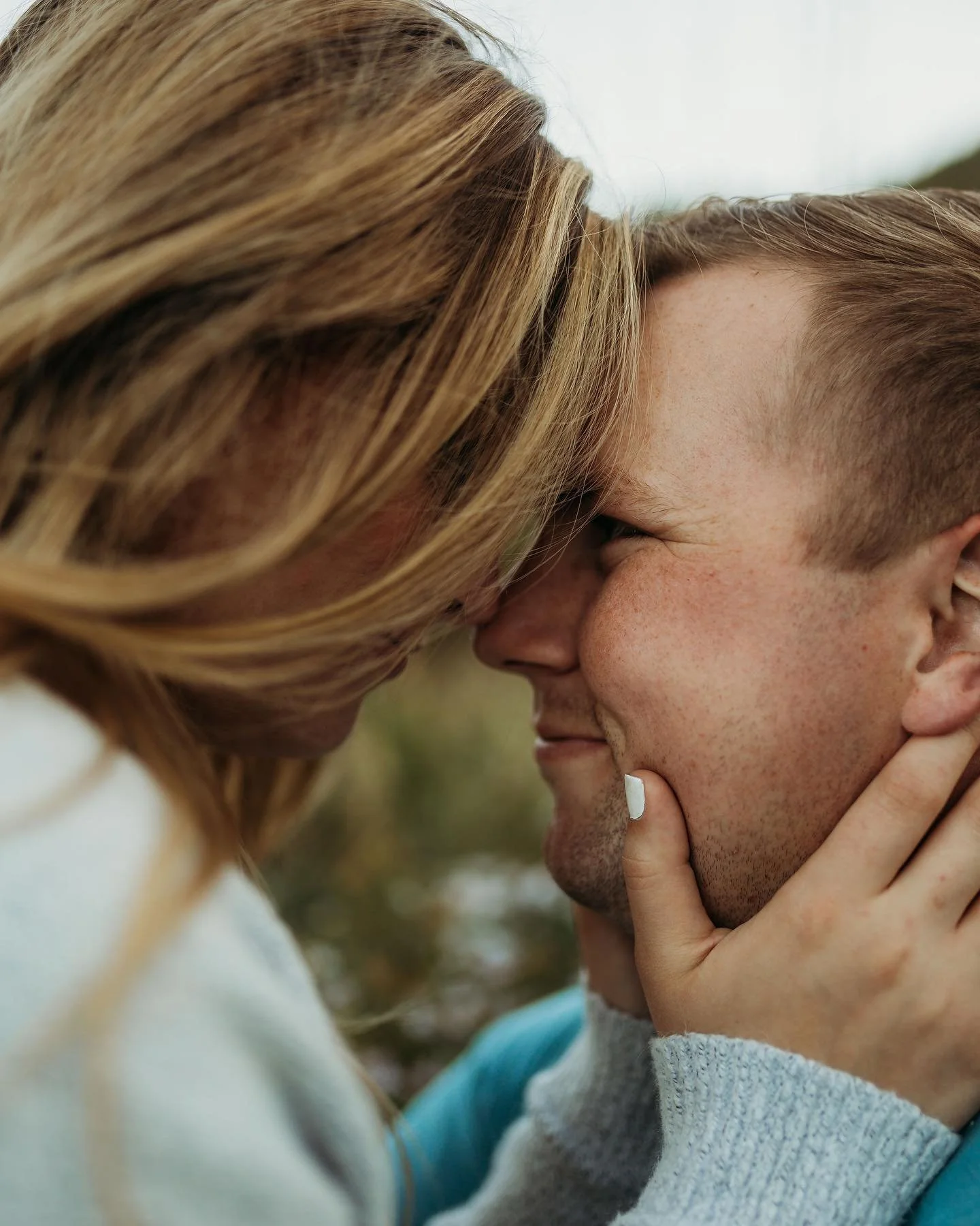 A close-up of a couple with their foreheads touching, smiling, and embracing outdoors.