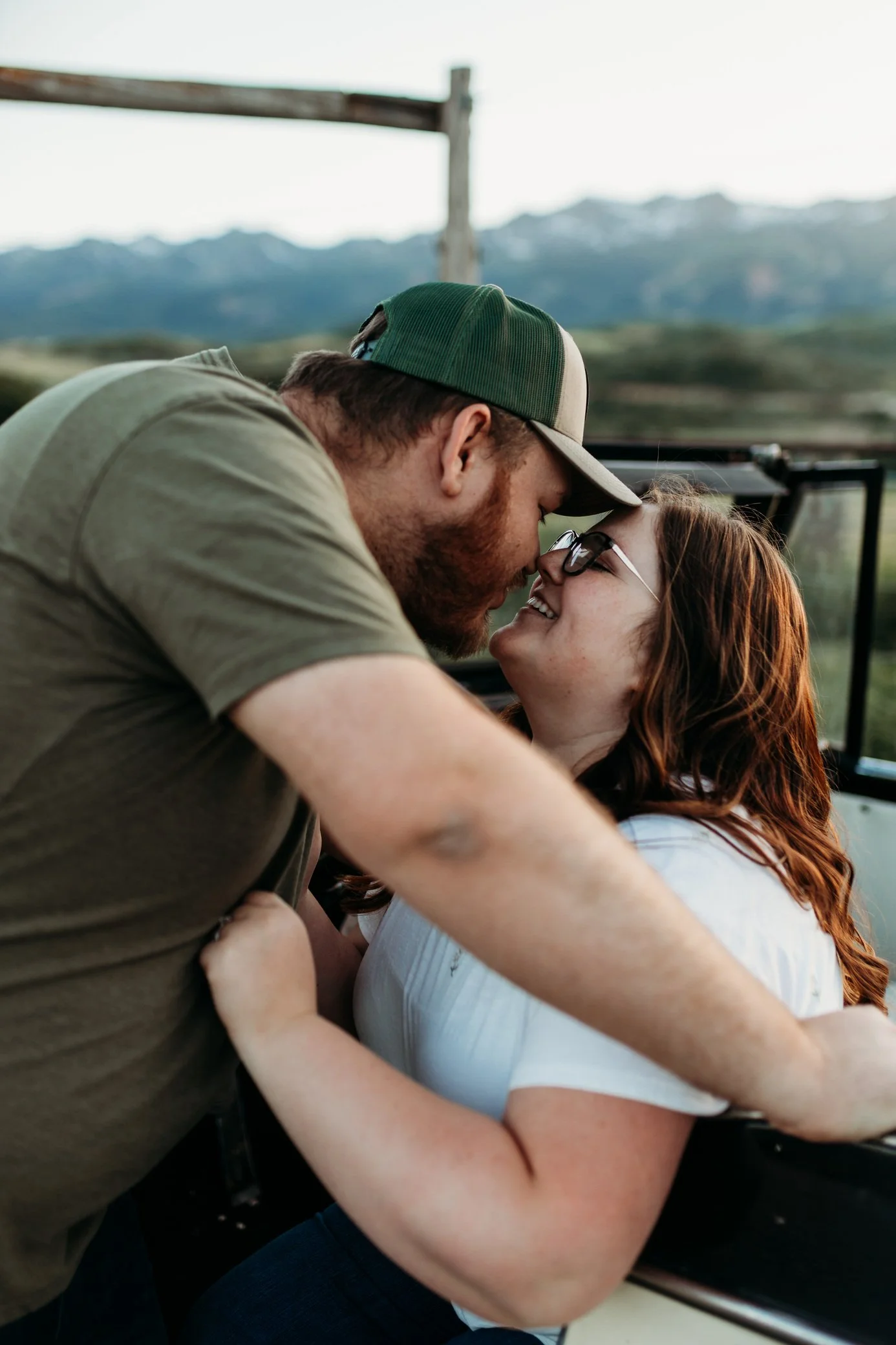 A couple sharing a romantic moment outdoors, about to kiss, with mountains in the background.