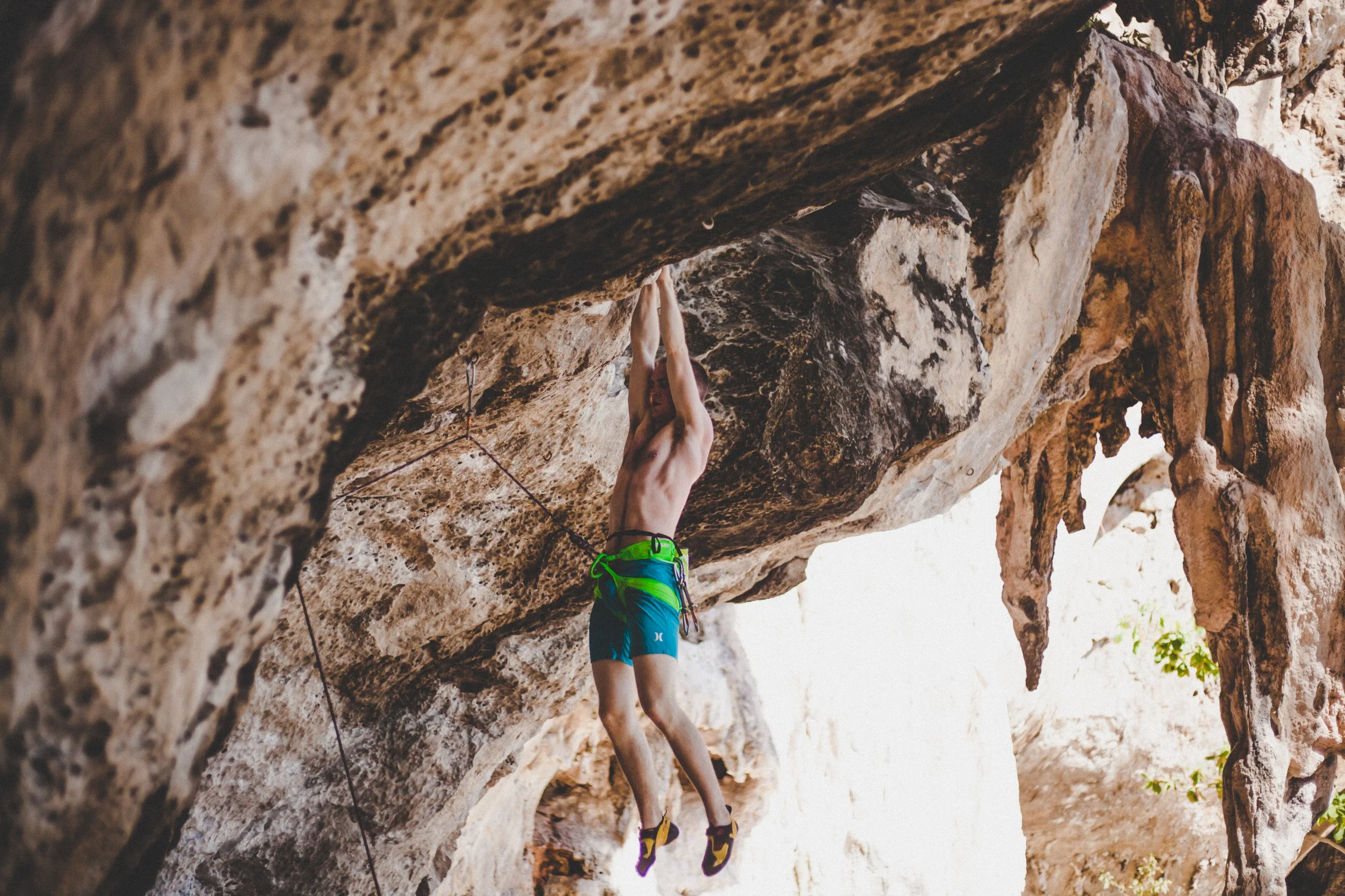 A man rock climbing on an overhanging indoor or outdoor rock wall, wearing a harness and climbing shoes.