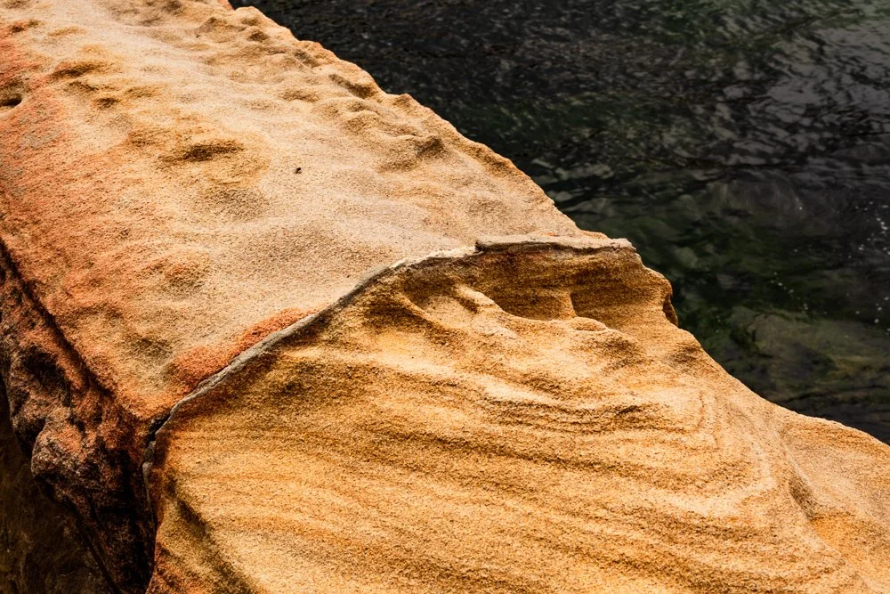 Close-up of an orange sandstone rock by dark water.