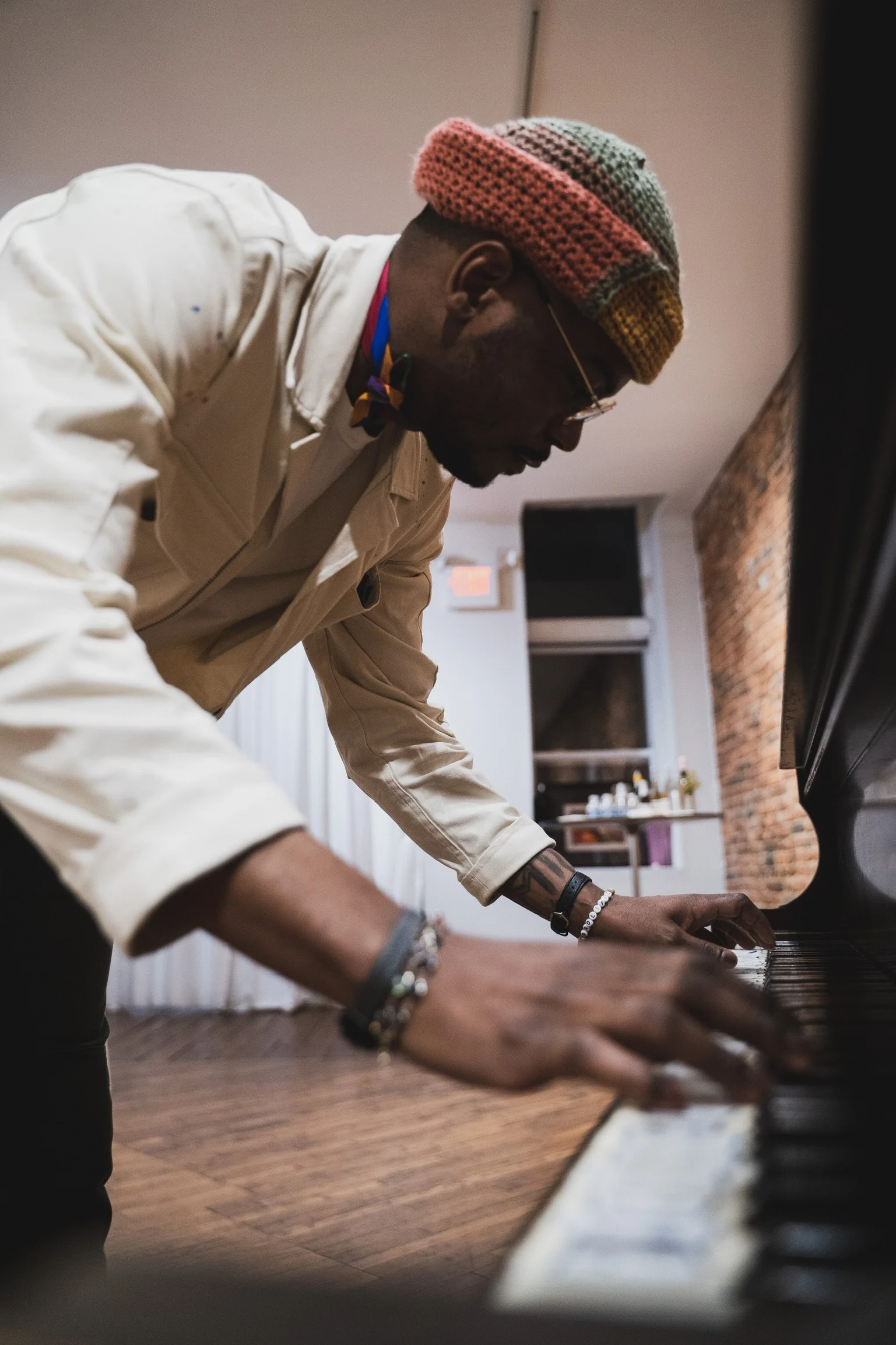 A man wearing glasses and a colorful knit hat playing a piano indoors.