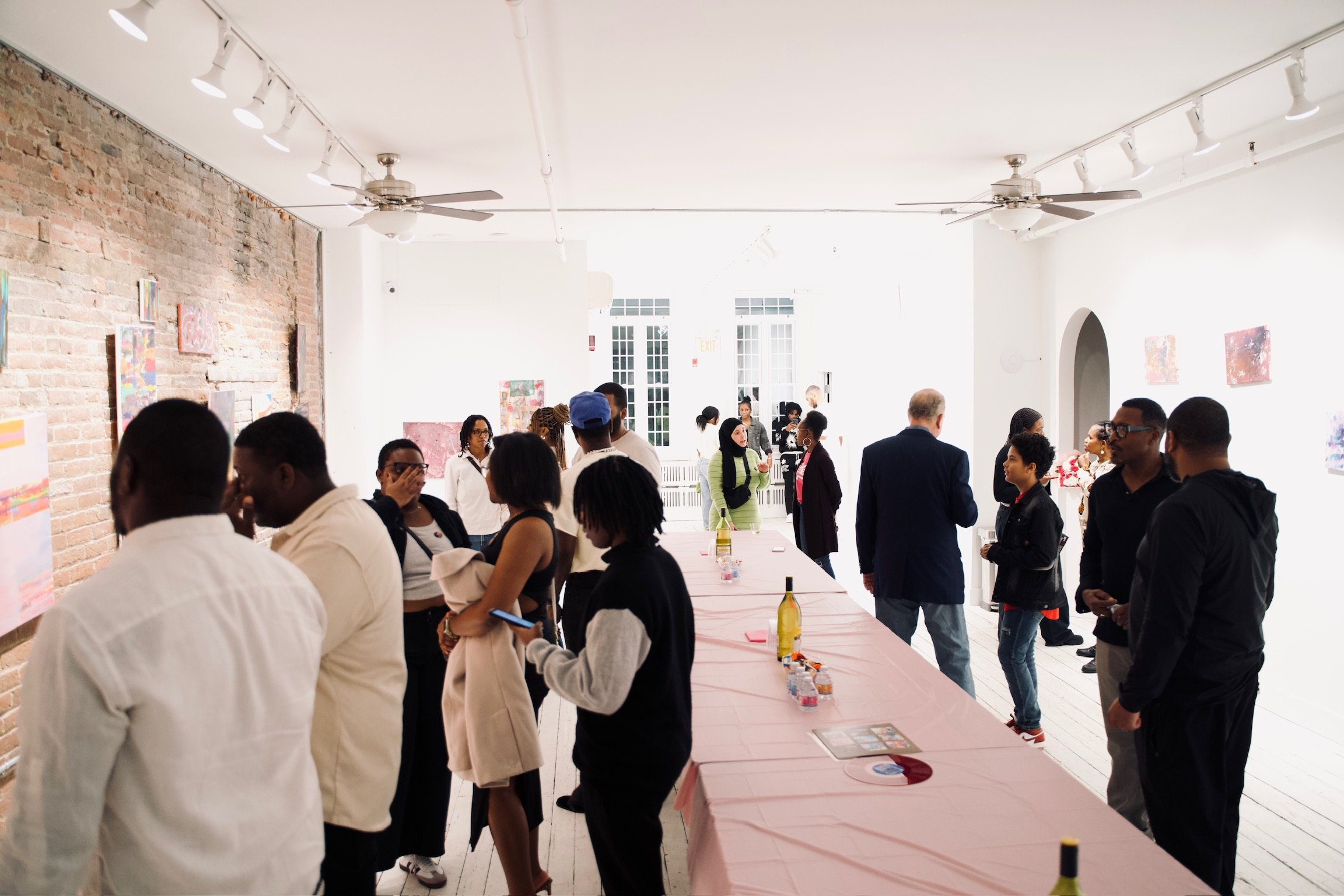 People at an art gallery or exhibition, mingling and viewing artwork on the walls.