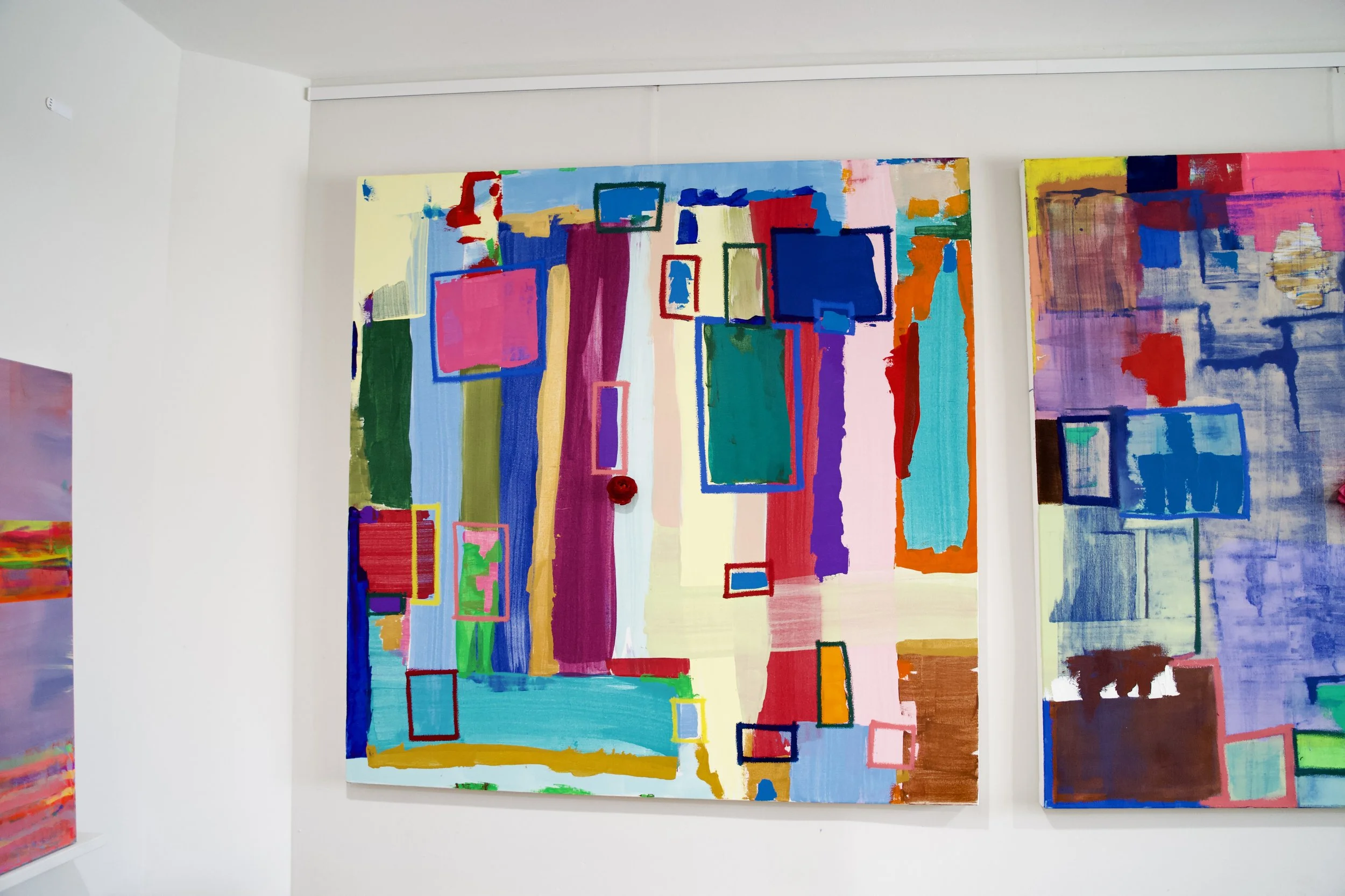 Abstract colorful painting on a white gallery wall with various shapes and rectangular outlines.