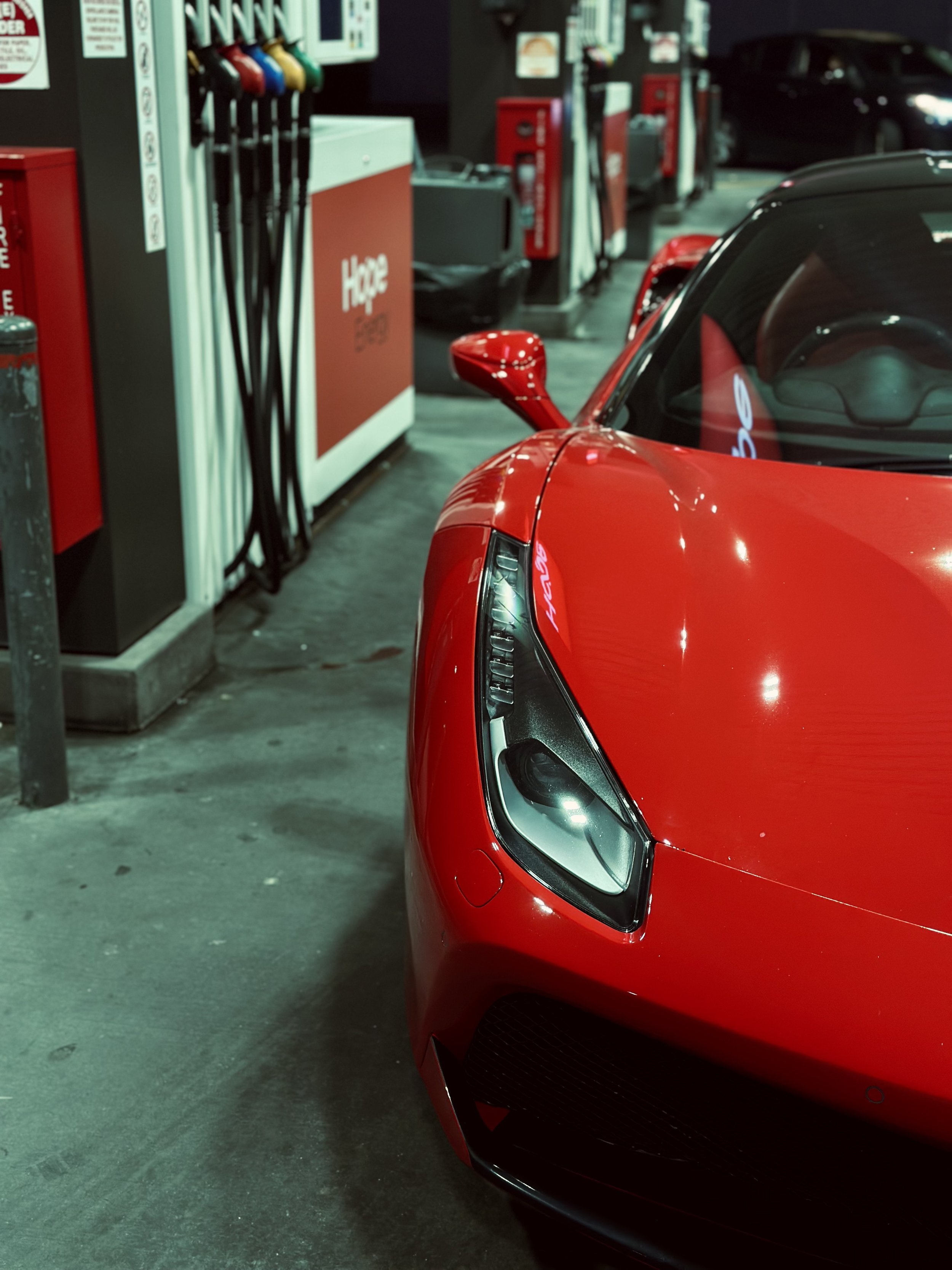 Red sports car at a gas station with fuel pumps in the background.