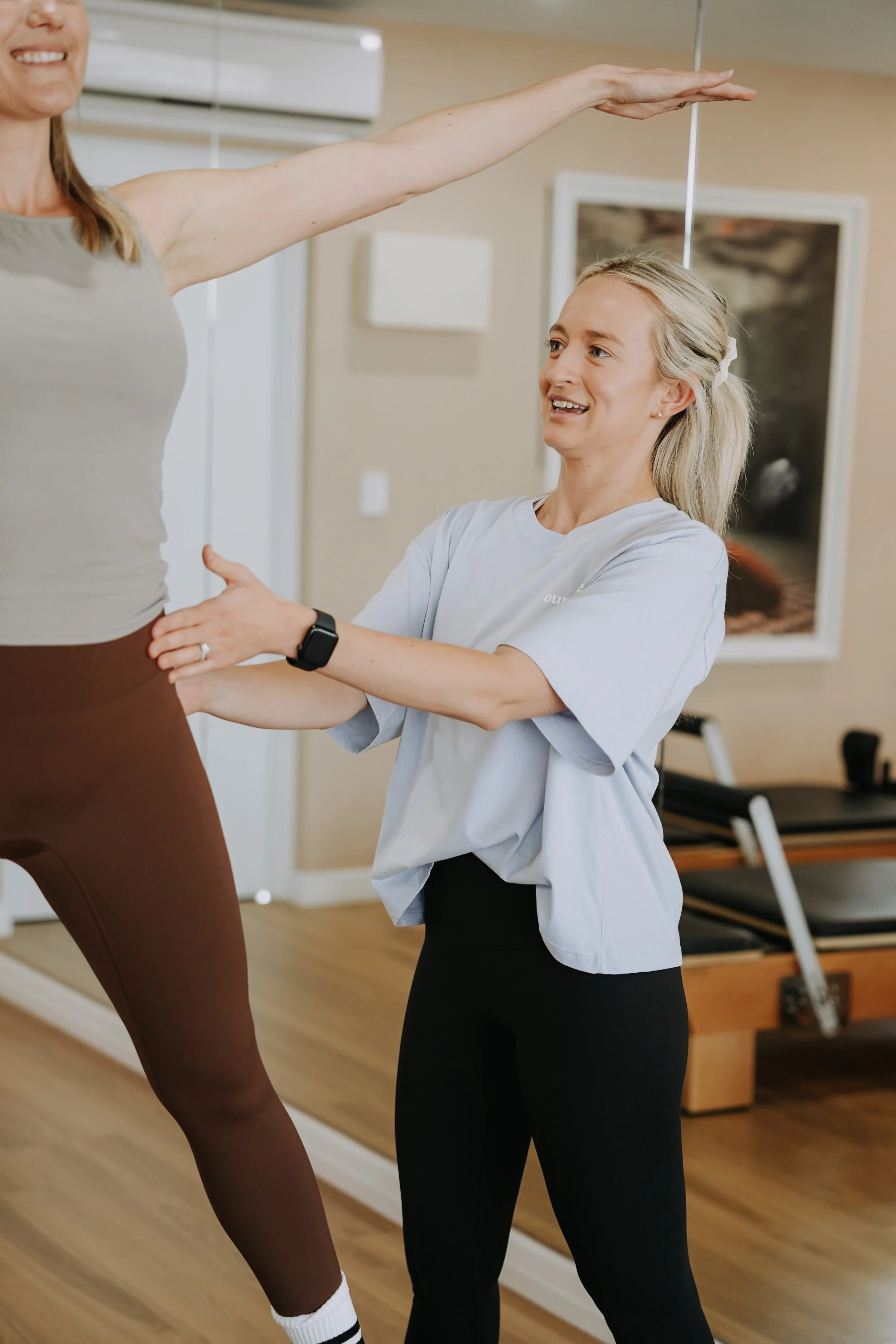 A physical therapist helps a woman with balance exercises while standing on a trampoline in a gym.