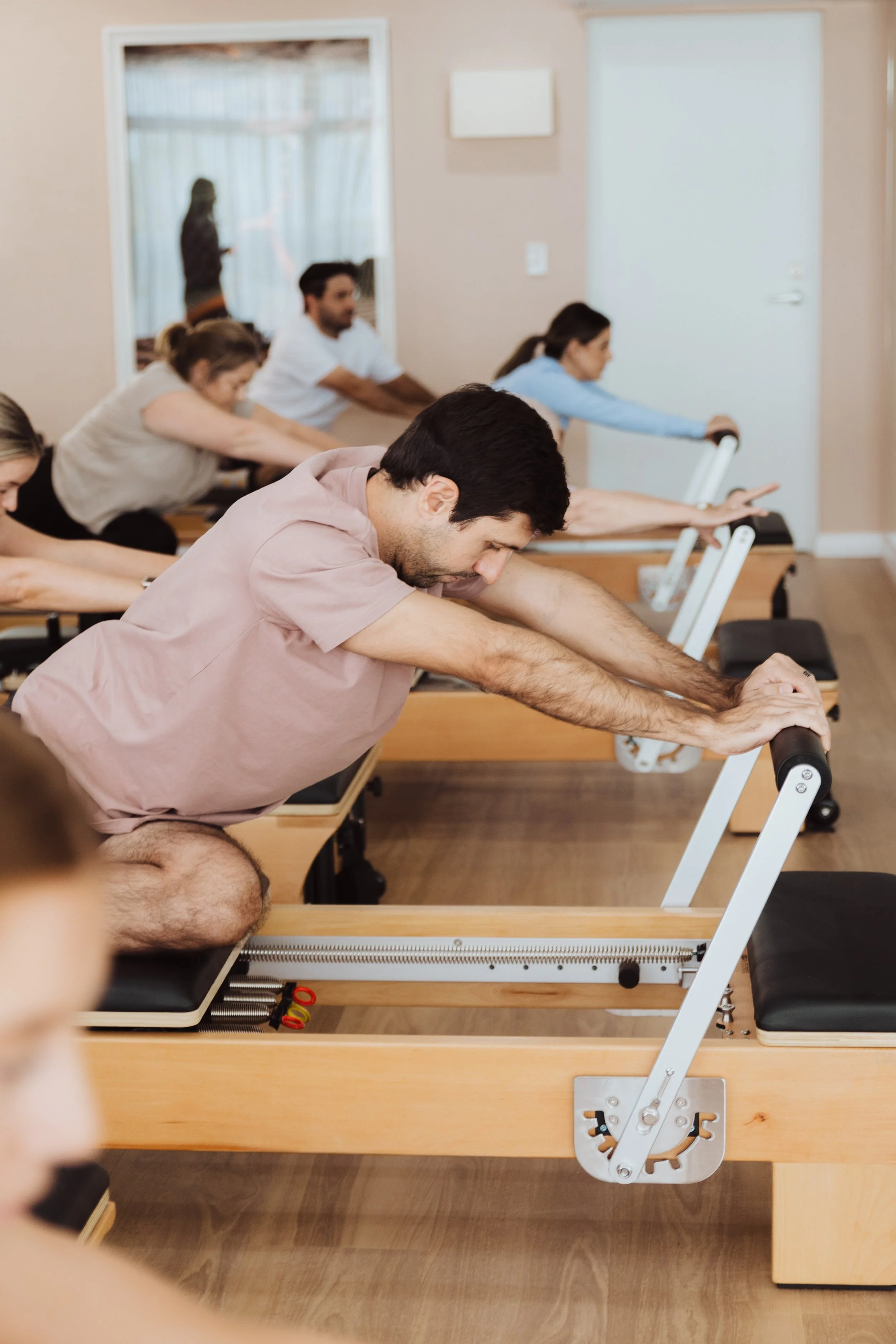 People exercising on Pilates reformer machines in a gym class, with focused expressions.