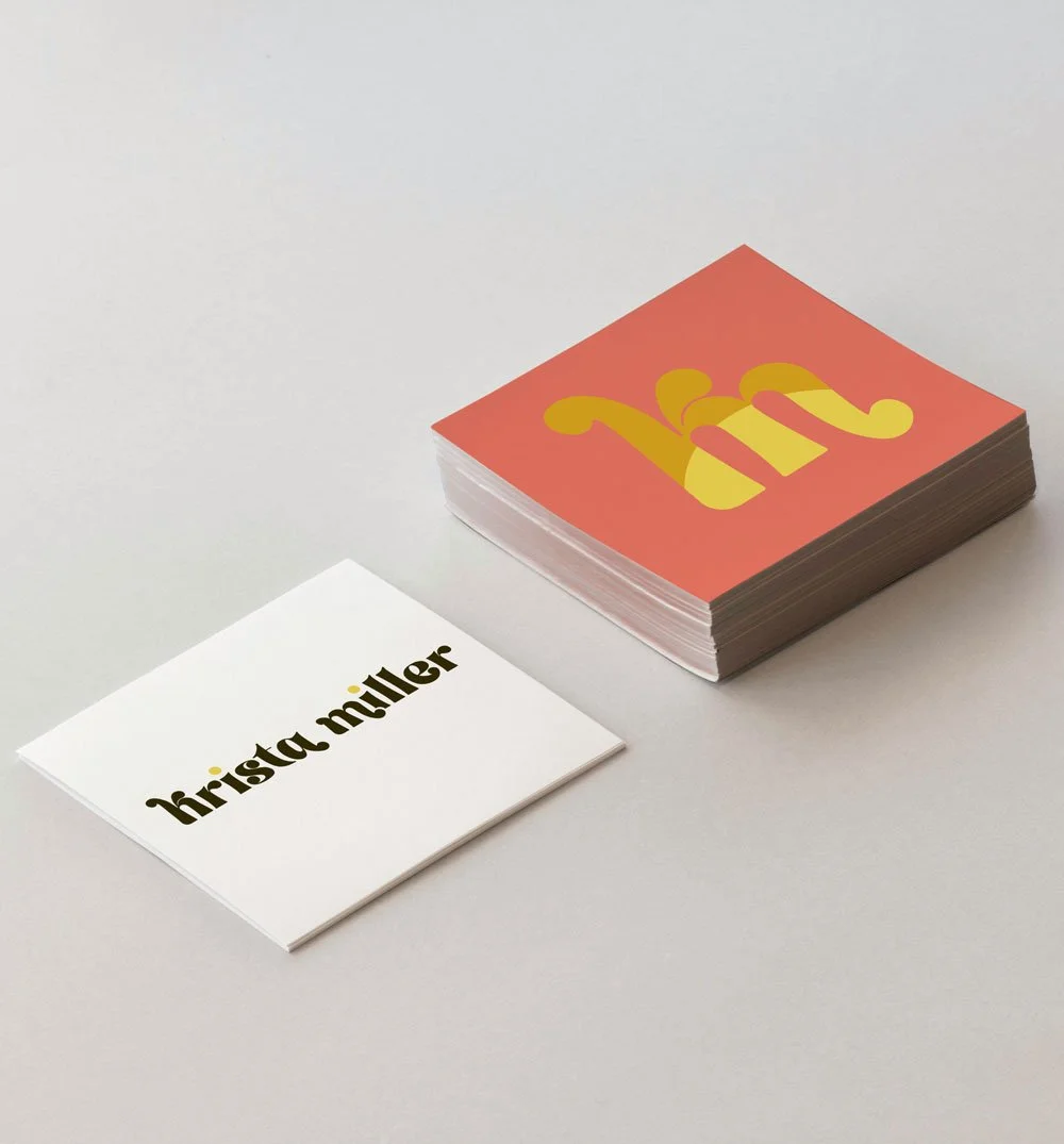A stack of business cards with the name 'Krista Miller' on a white card, and a separate stack with a red and yellow logo.