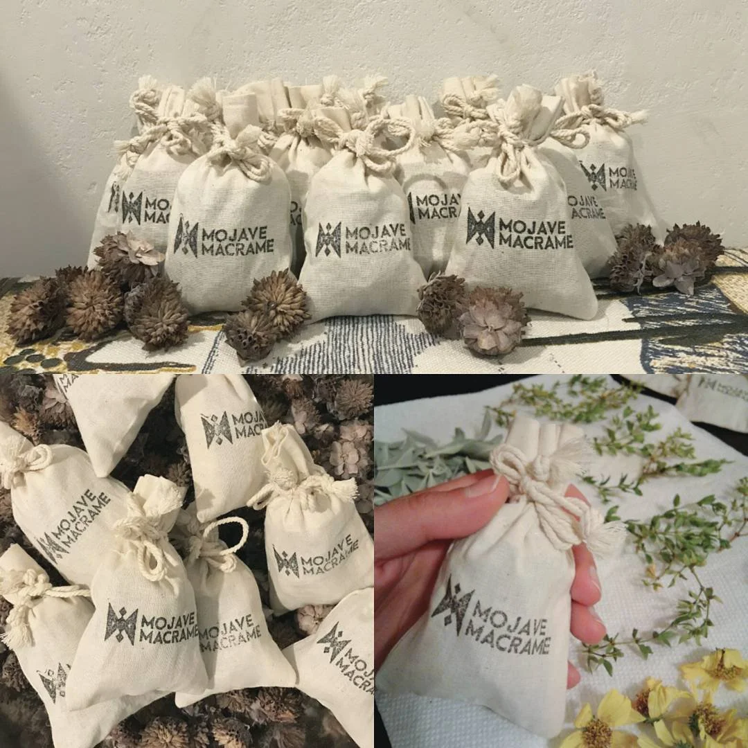 Multiple small white fabric bags with the 'MOJAVE MACRAME' logo, tied with knots, surrounded by dried flowers and plants.