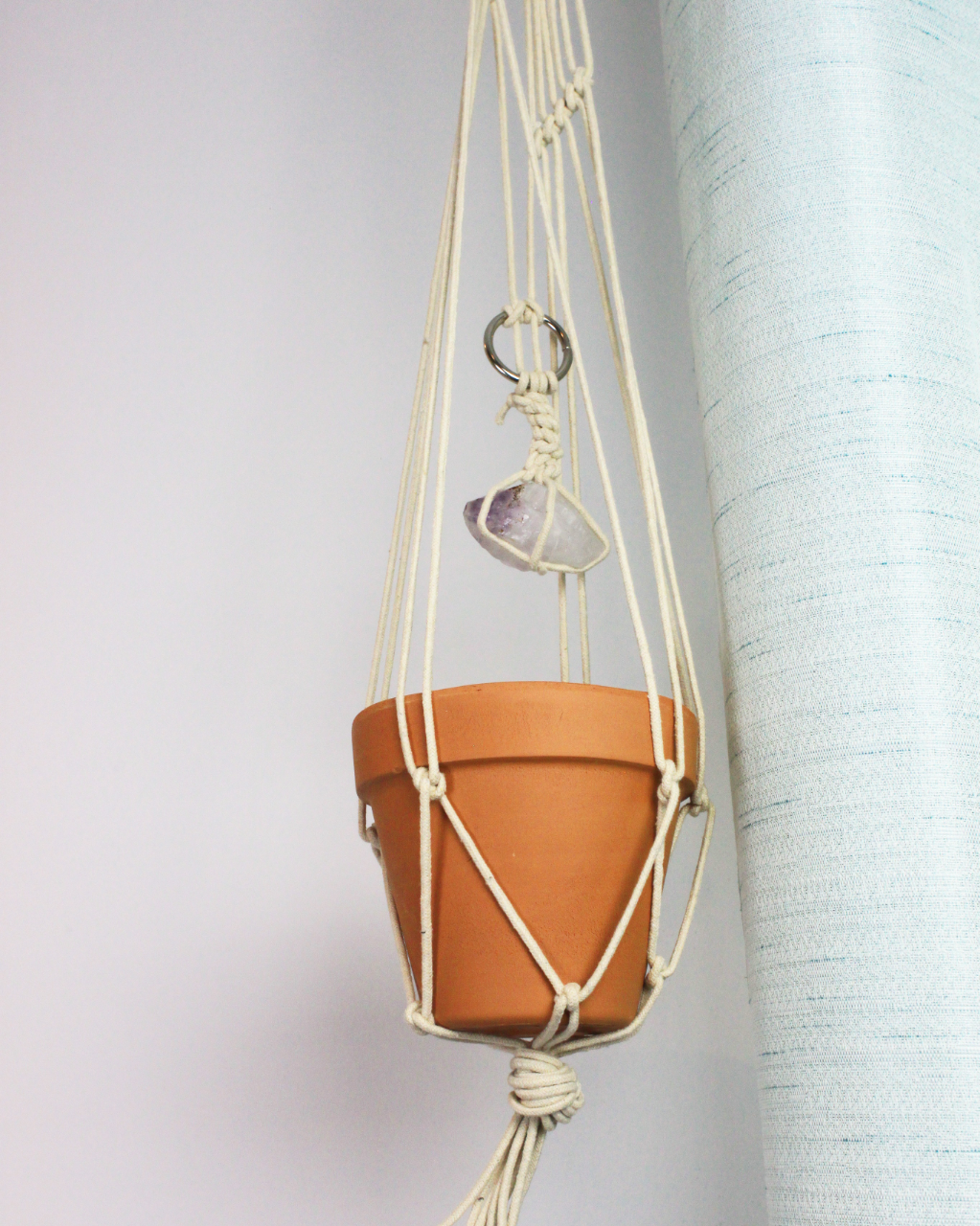 Hanging plant with a terracotta pot in a macrame holder and a piece of amethyst attached to the strings.