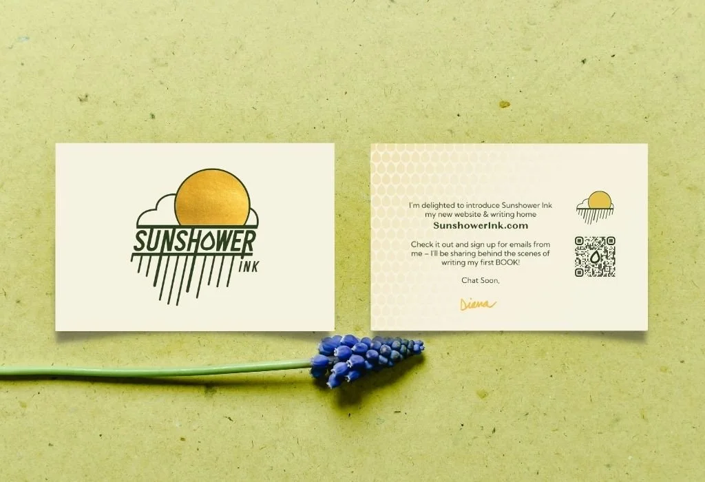 Business card with a sunny logo and the text 'Sunshower Ink' on a light green background, next to a sprig of purple grape hyacinth flower.