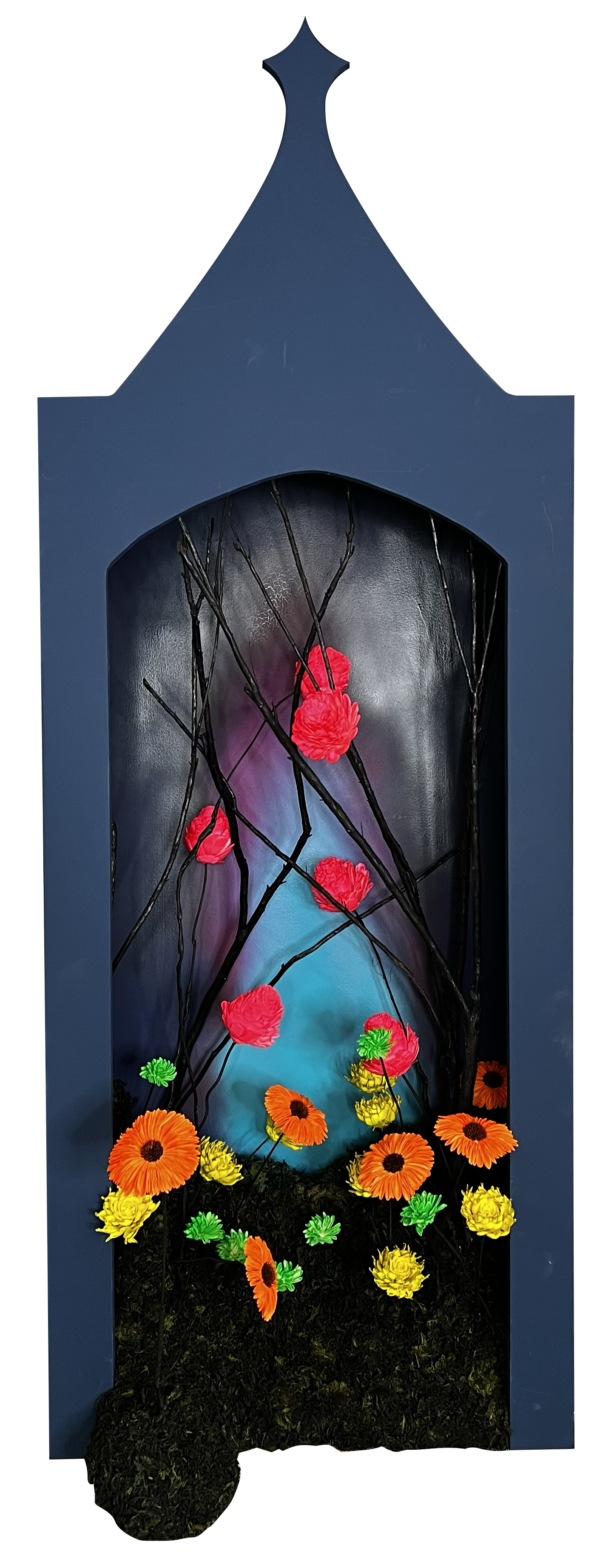 Colorful art display inside a structured frame, featuring black branches, vibrant red, yellow, orange, and green artificial flowers, with a glowing blue backdrop and a dark mossy base.