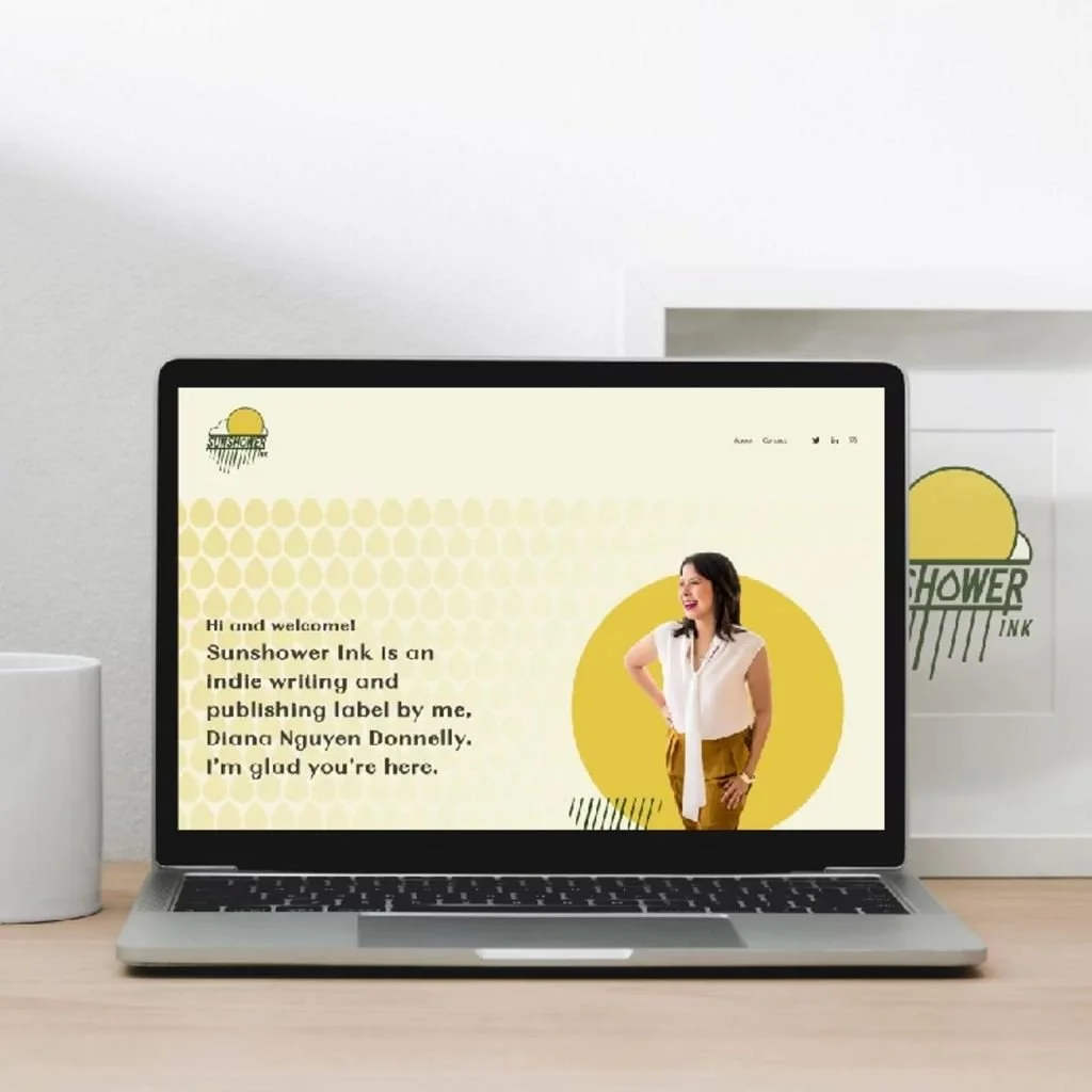 A laptop on a wooden desk displaying a website with an introduction to Sunshower Ink, an indie writing and publishing label by Diana Nguyen Donnelly, featuring a woman with dark hair smiling and standing against a yellow circle background.