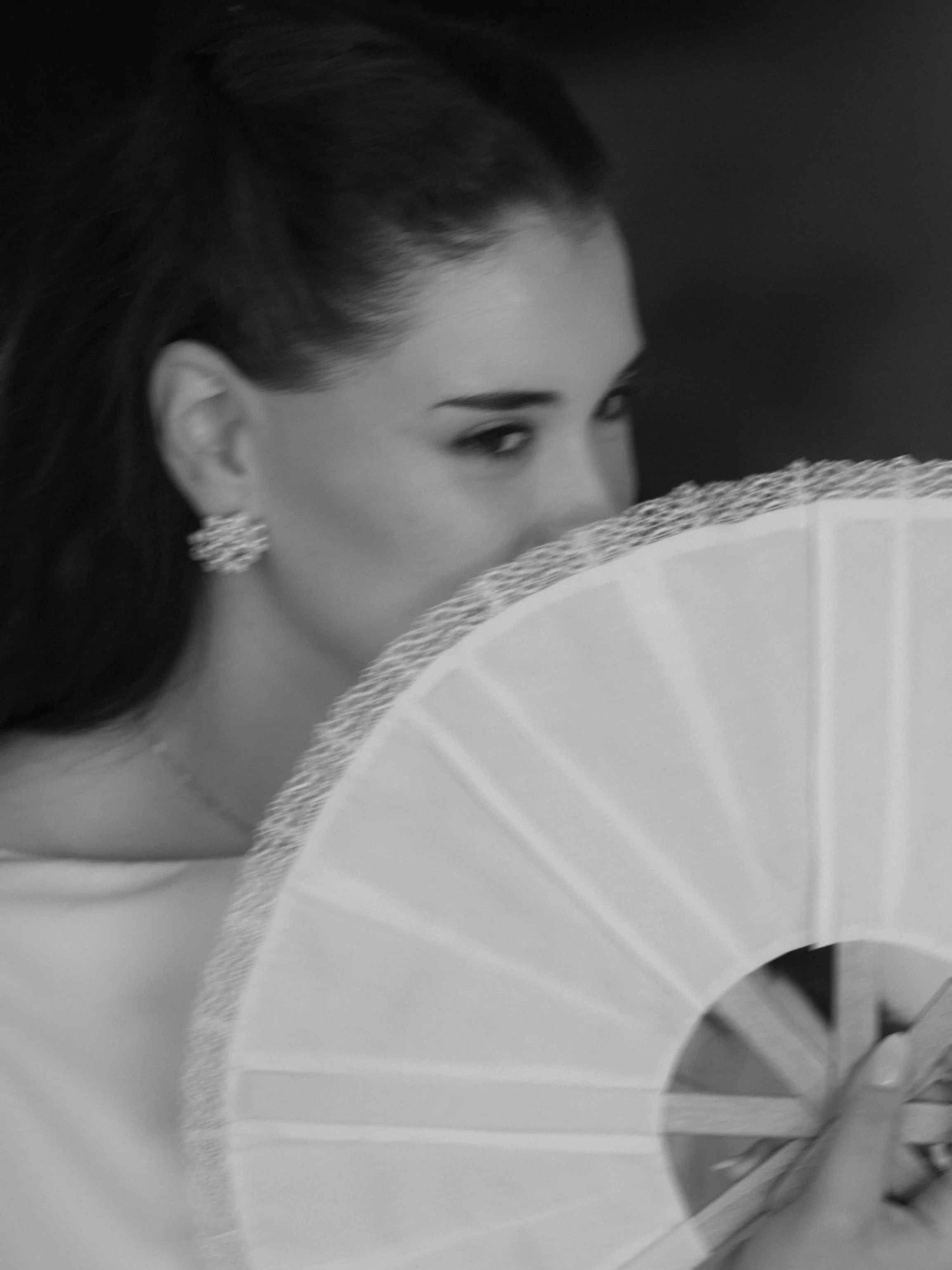 Retrato artístico en blanco y negro de una novia con cabello oscuro semi oculta tras un abanico de encaje.