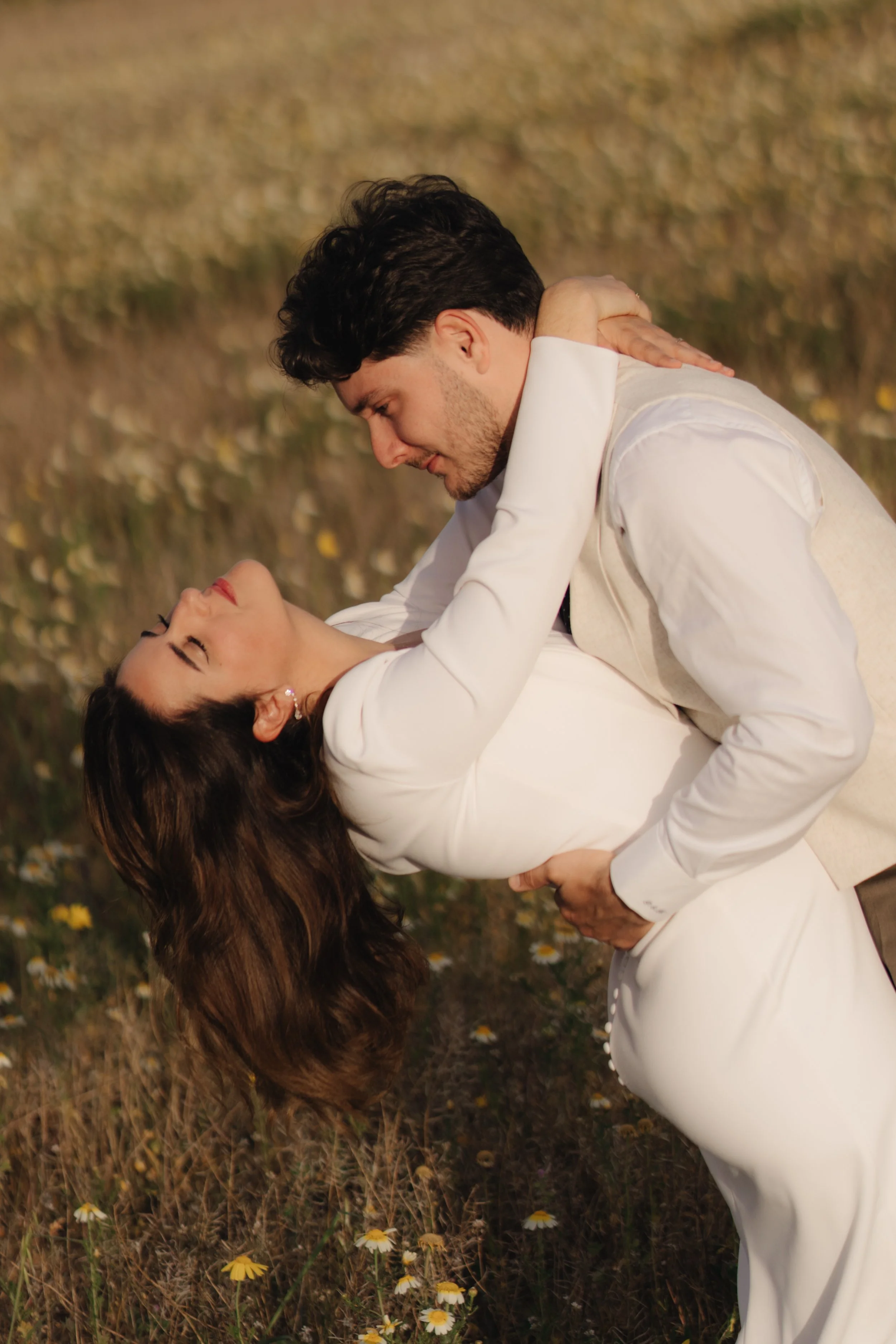 Una pareja bailando en un campo de flores, con el hombre inclinado y la mujer inclinada hacia atrás, ambos con expresión de felicidad.