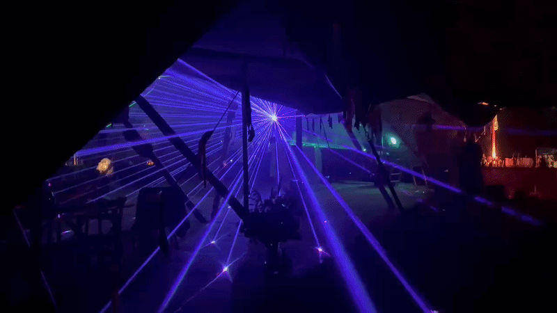 A dark scene at a party with purple and blue laser lights projected onto the ceiling and walls.