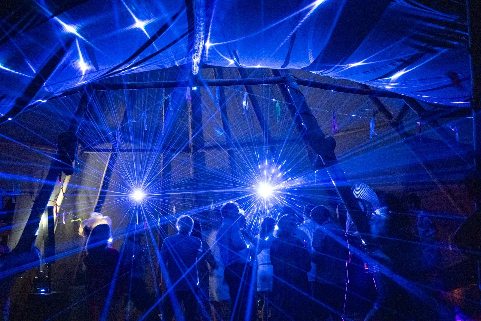 People at a laser light show with blue and purple laser beams and bright lights.