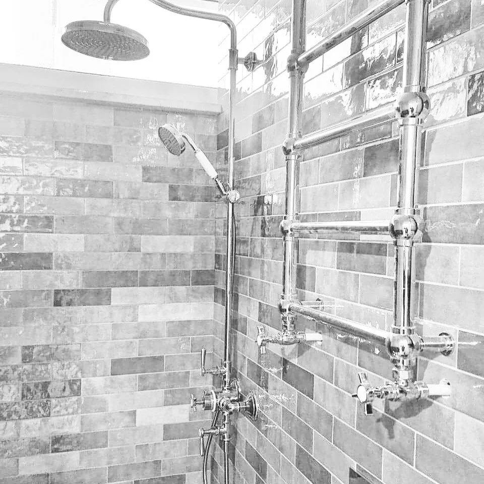 łazienka retro z ekskluzywną armaturą i stylizowanym chromowanym grzejnikiem. Bathroom shower with showerhead and a wall-mounted metal pipe radiator.